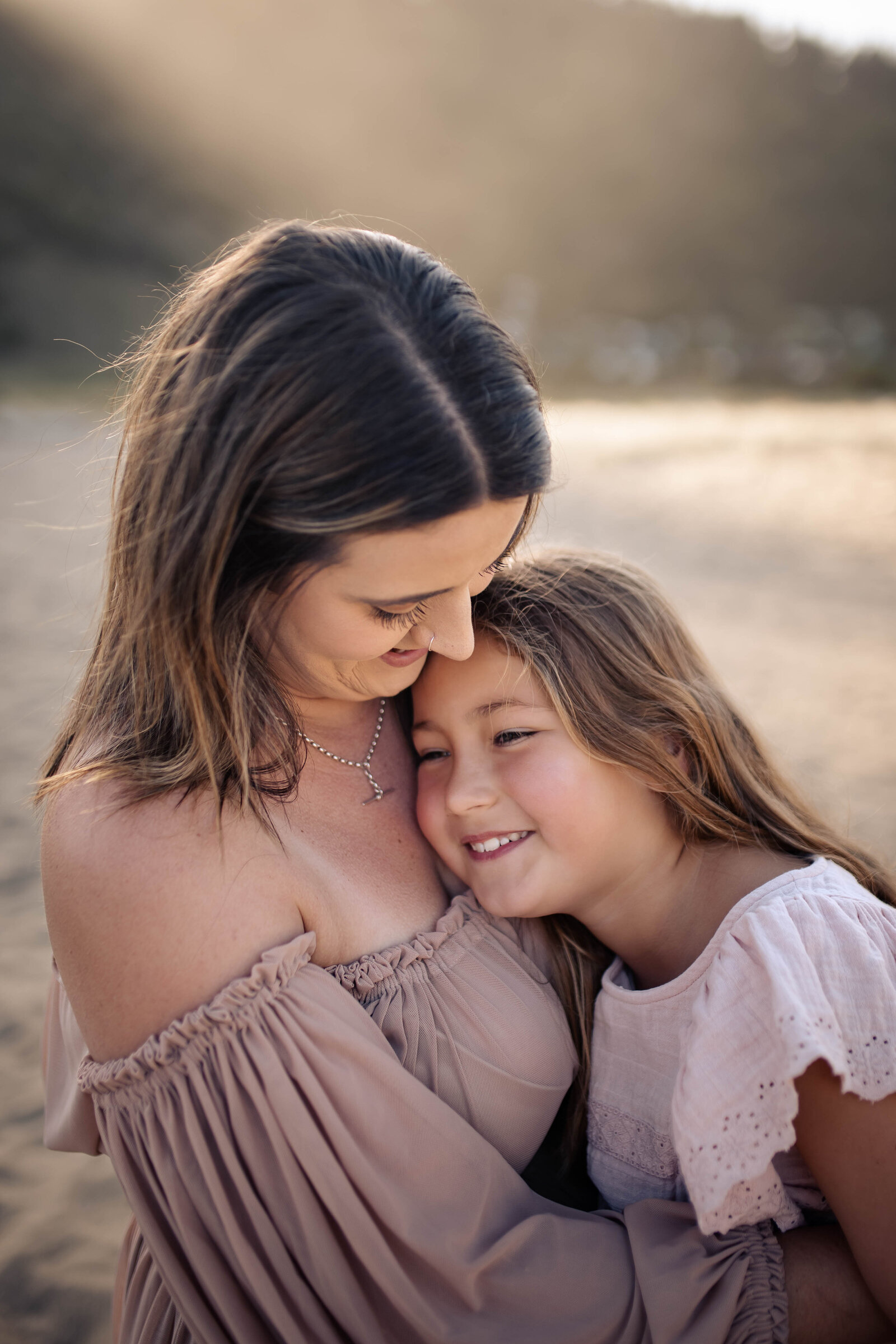 Mum cuddling her laughing 7-year-old daughter at Waipatiki Beach during golden hour – relaxed, joy-filled family photography in Hawke’s Bay.