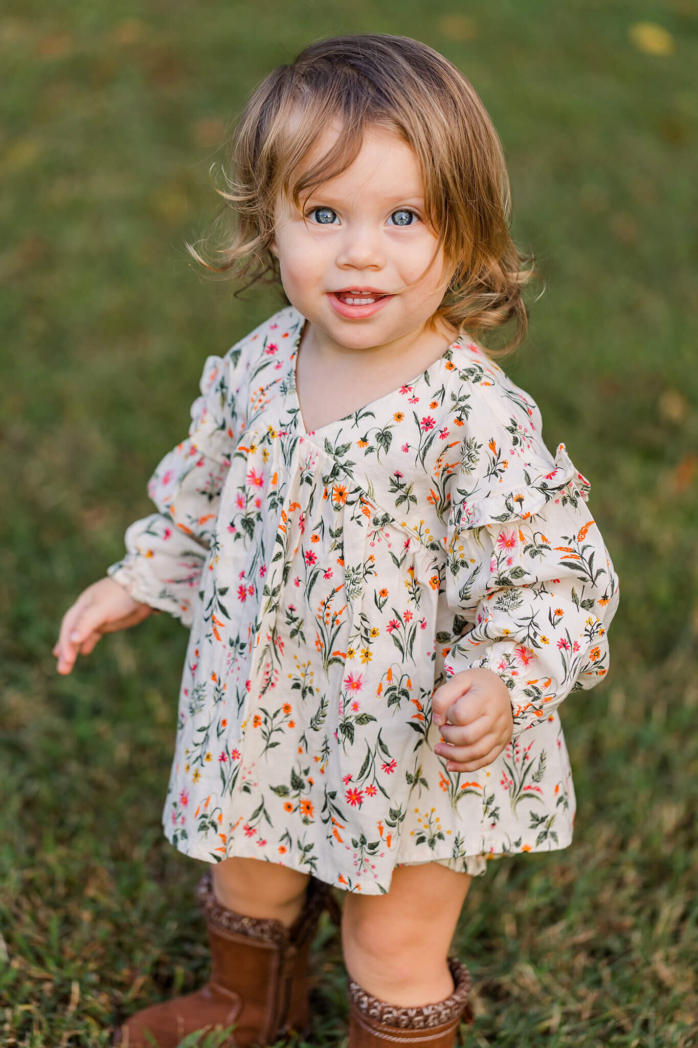 A little girl standing in the grass in a floral romper during a family photography session in a park in Northern Virginia.