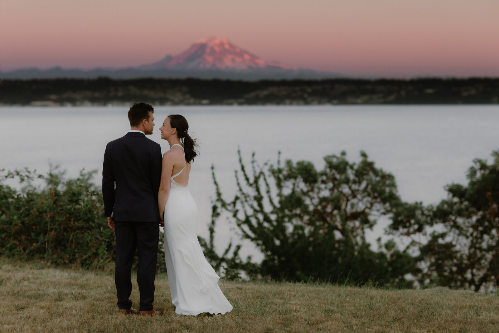 Bride and groom at sunset standing in a field on Vashon Island with Mount Rainier visible in the background.