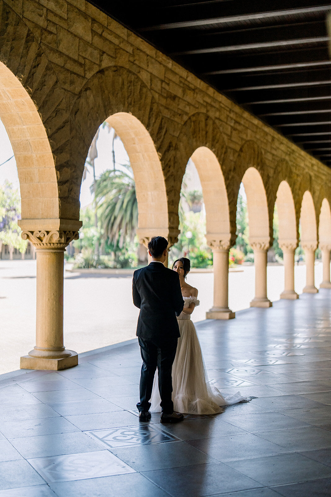 The groom stands in anticipation, waiting for his bride under the historic arches of Stanford University.