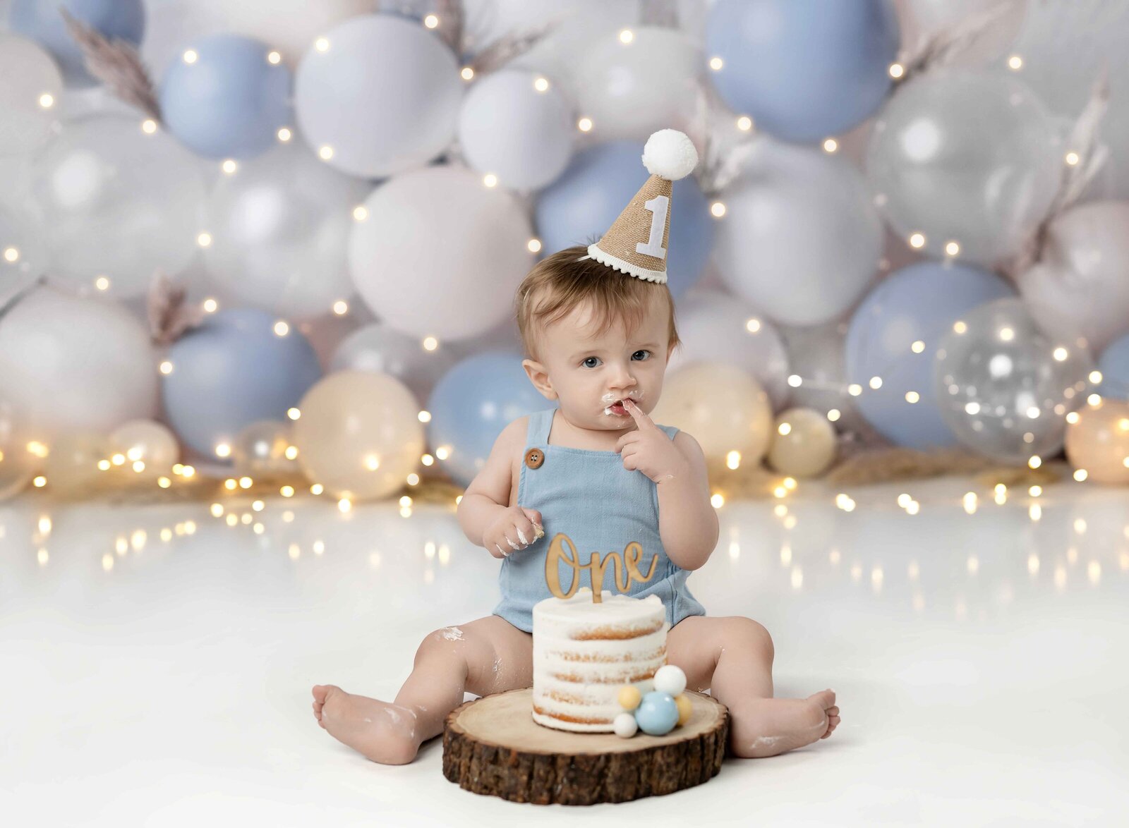 Baby boy in blue romper tasting birthday cake for the first time. Photographed at Atlanta cake smash photo studio.