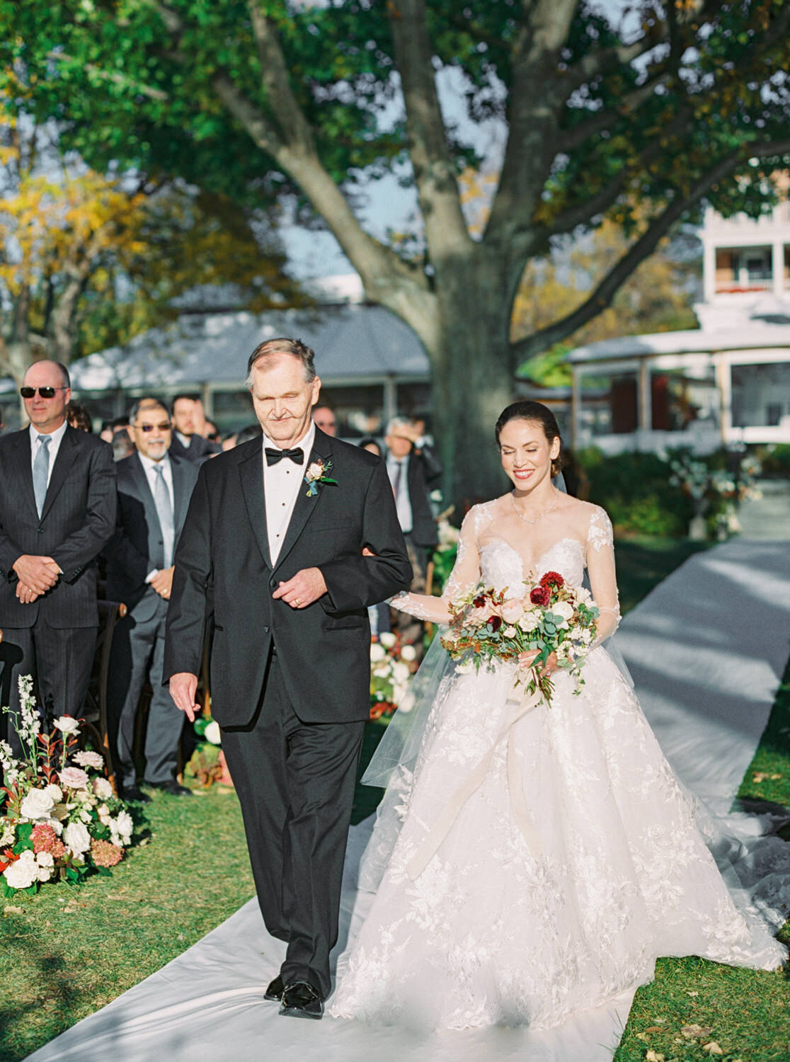 Bride and her father walking down the aisle with Inns of Aurora in the background.