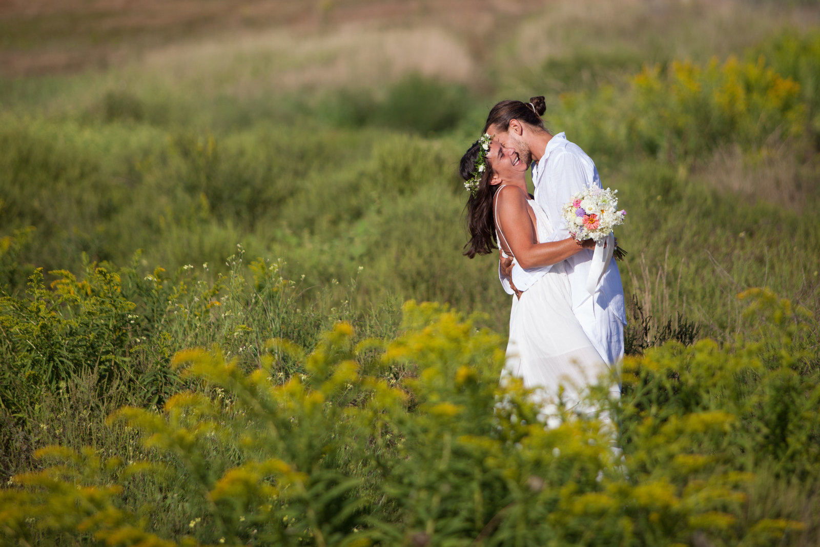 Bride and groom kissing in field of grass