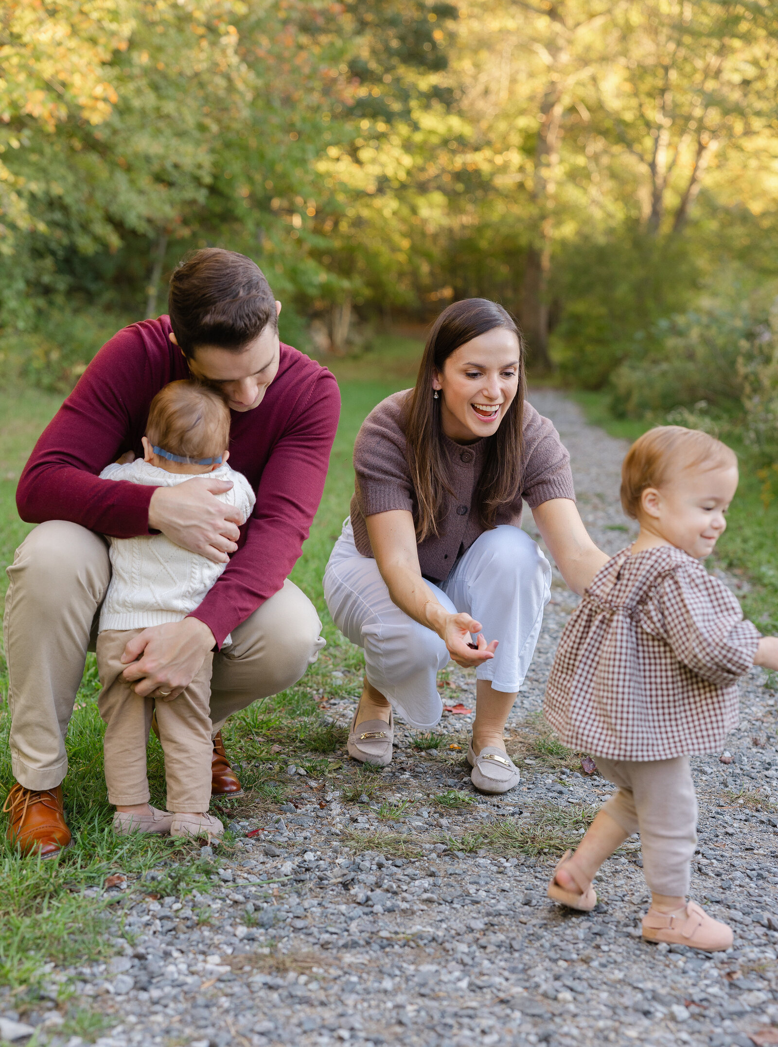 Parents crouch to play with their two toddlers on a gravel path surrounded by autumn trees, photographed by a Central Massachusetts family photographer
