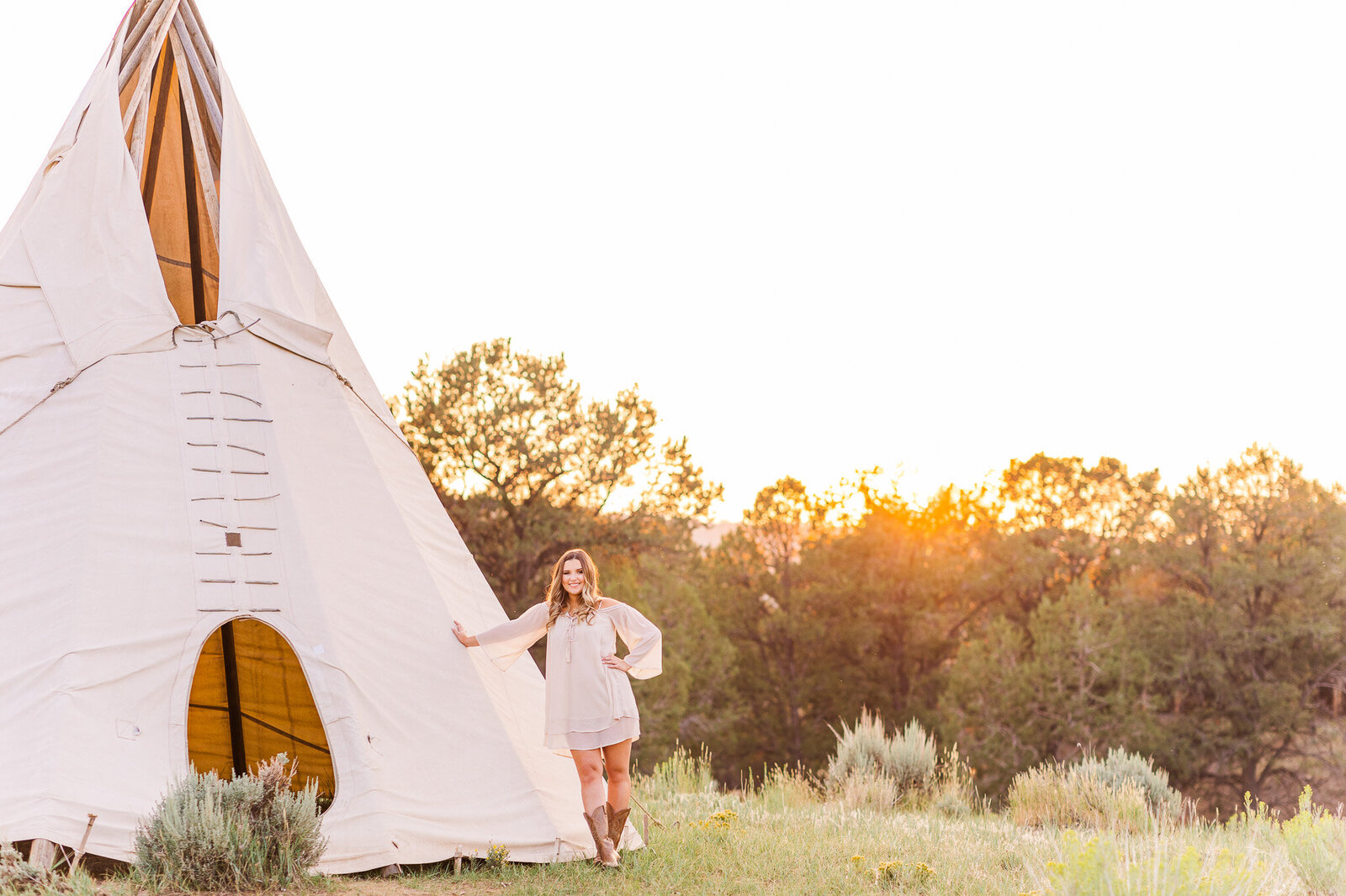 sunset behind subject as she stands against a teepee