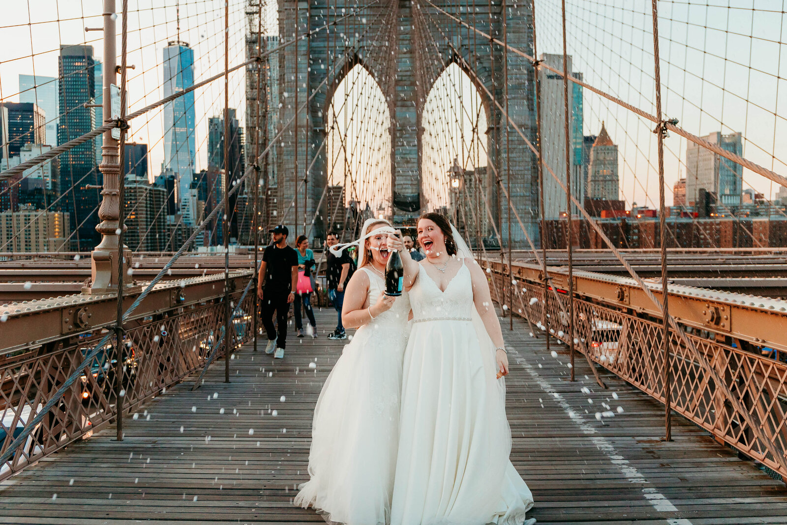 two brides pop champagne on brooklyn bridge