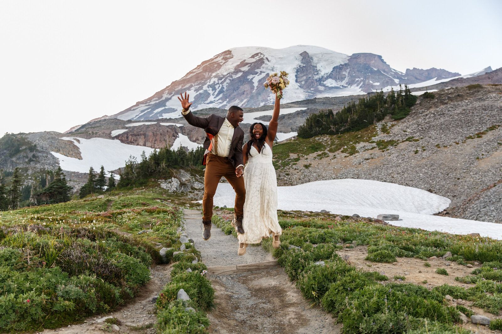 a bride and groom jump on a trail in mount rainier national park