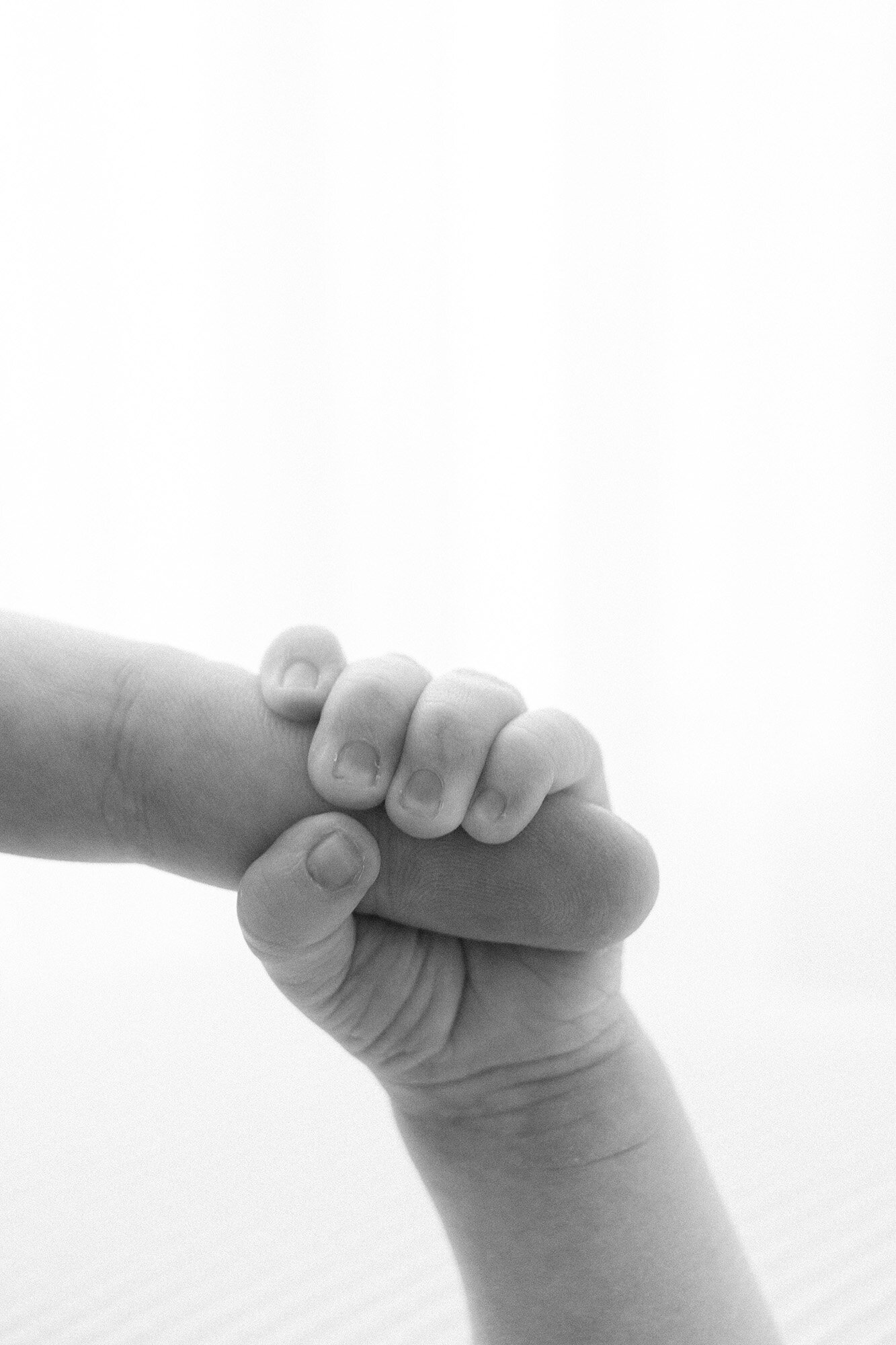 newborn baby's hand wrapped around dad's finger in black and white