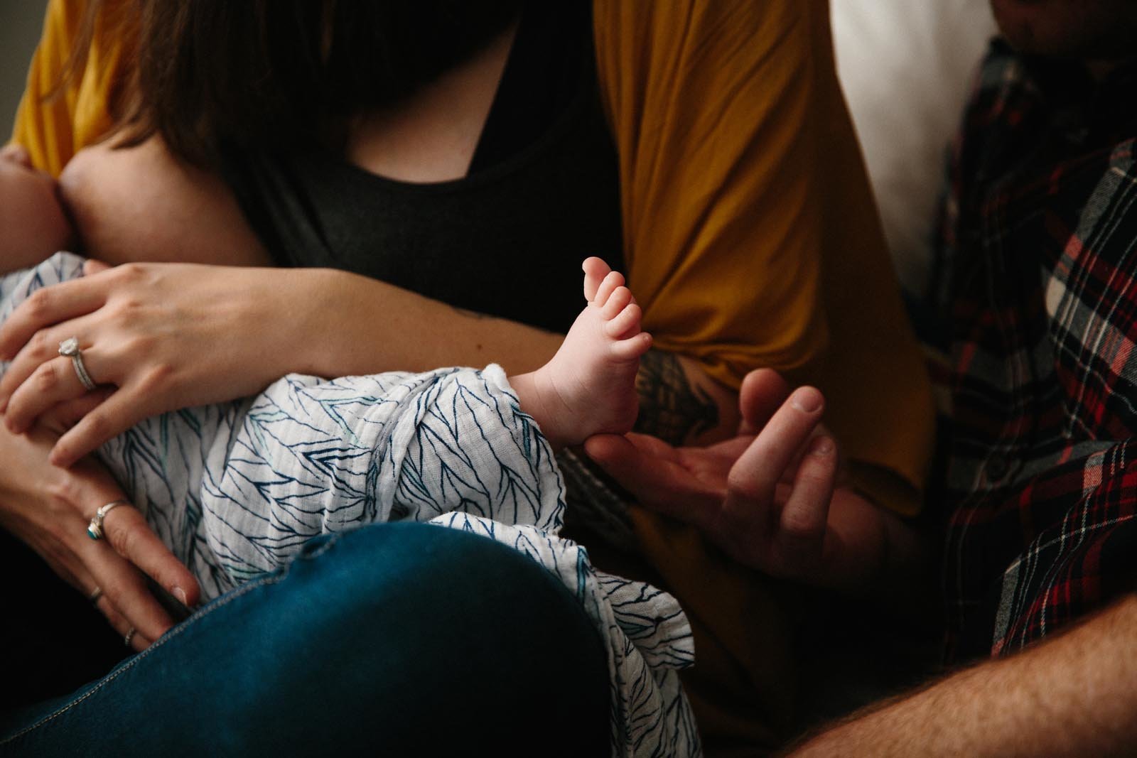 close up of mom and dad sitting close together with newborn baby and dad touching his son's tiny foot