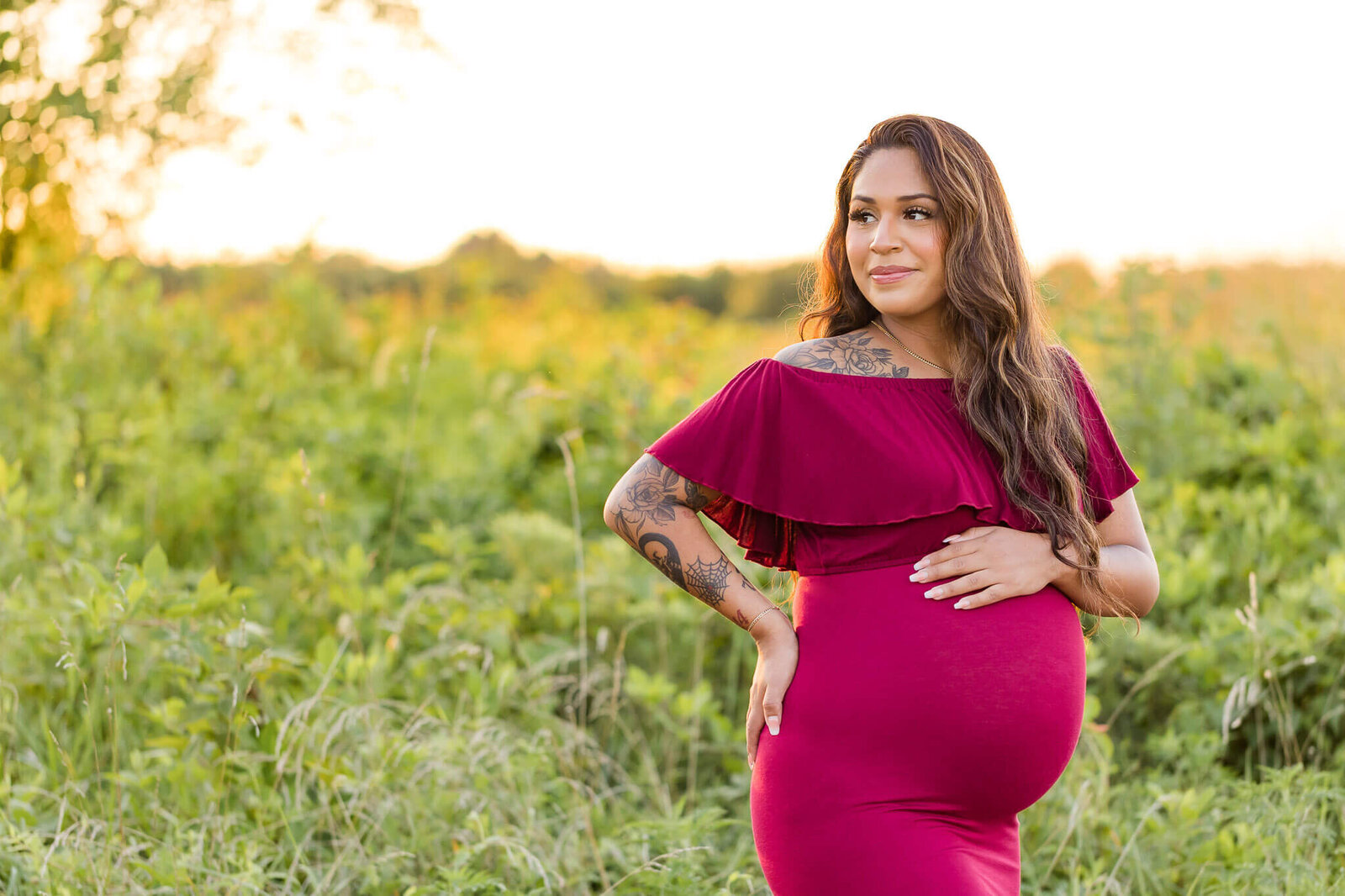 A mom-to-be posing in a red dress and looking off into the distance.