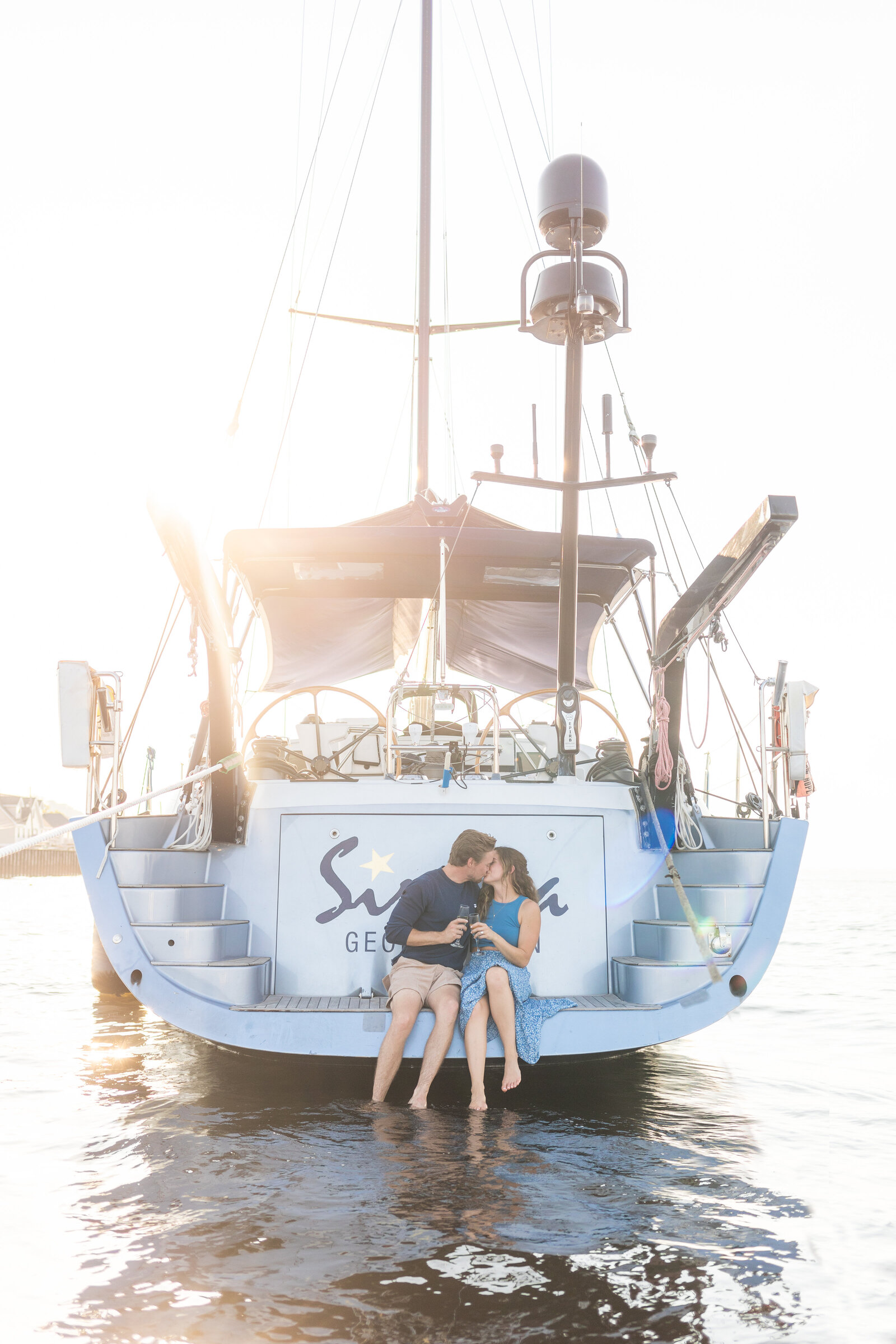 engaged couple sitting off yacht clinking champagne in sea bright