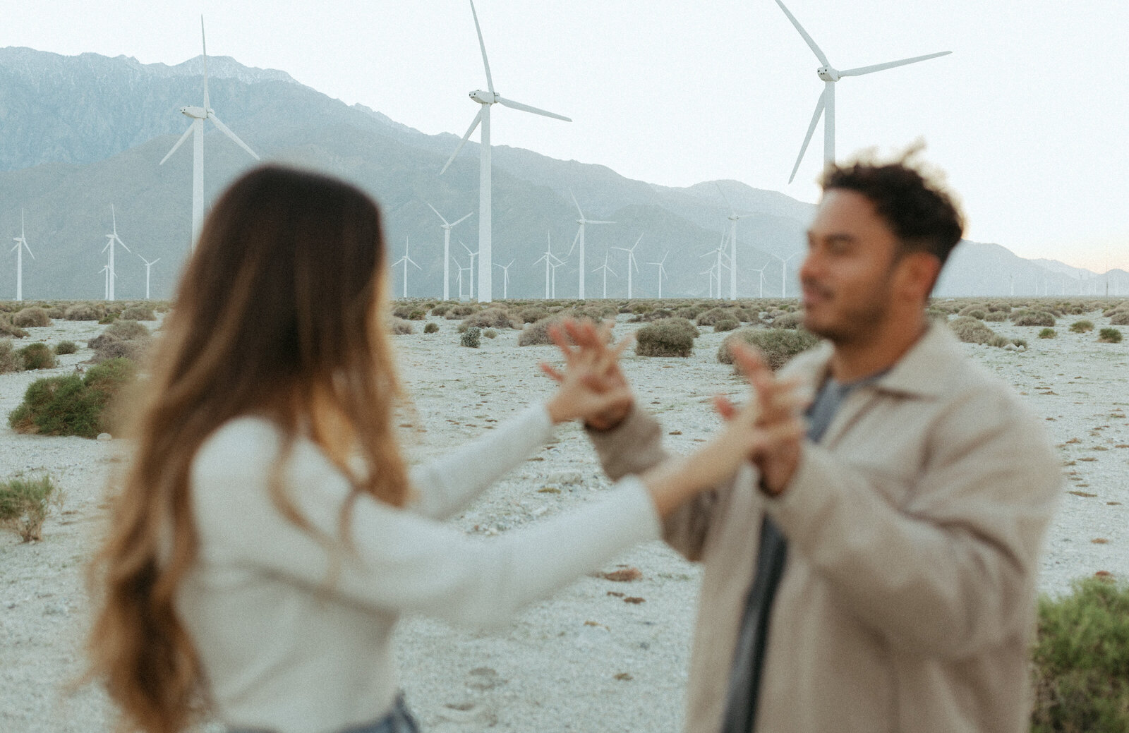 couple at the windmills in California holding hands facing each other