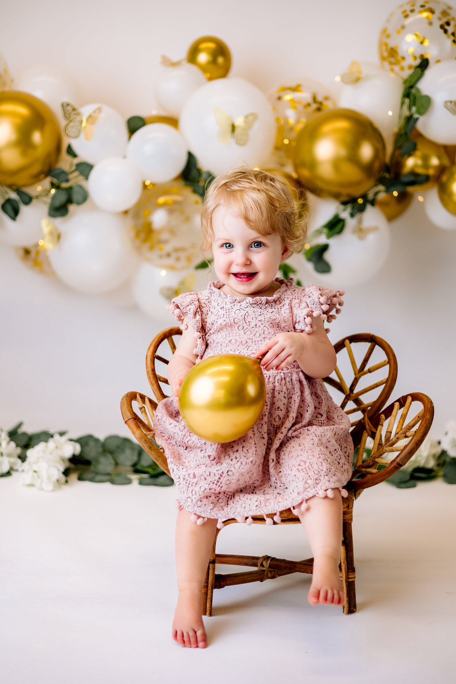 Sweet baby girl in a pink dress sits in an adorable rattan chair