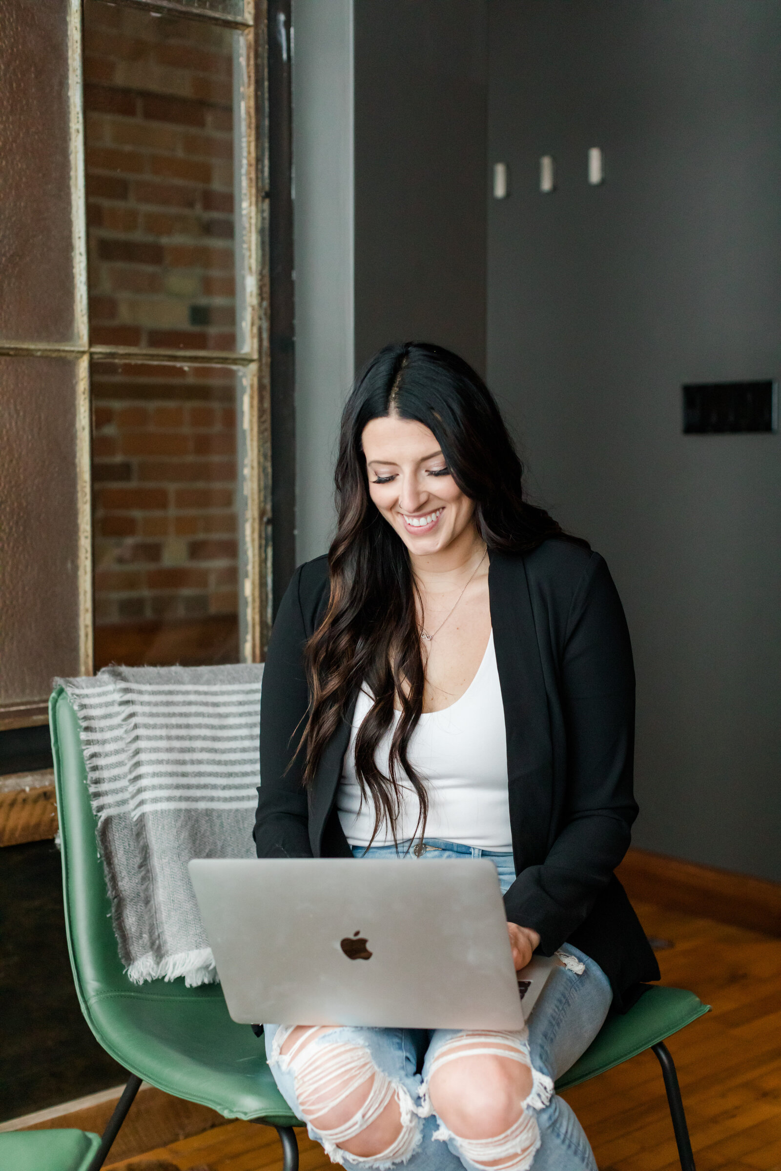 Portrait of Allie Clark, founder of Allie Clark Designs, smiling and holding a black coffee mug in a modern, industrial-style studio setting.