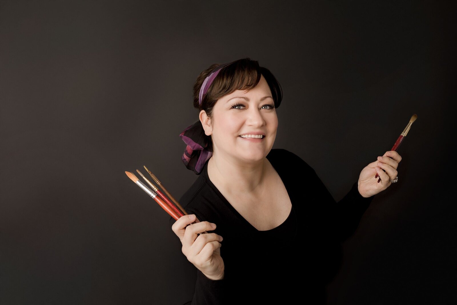 an artist holding brushes posing for a branding photo for her graphic design business