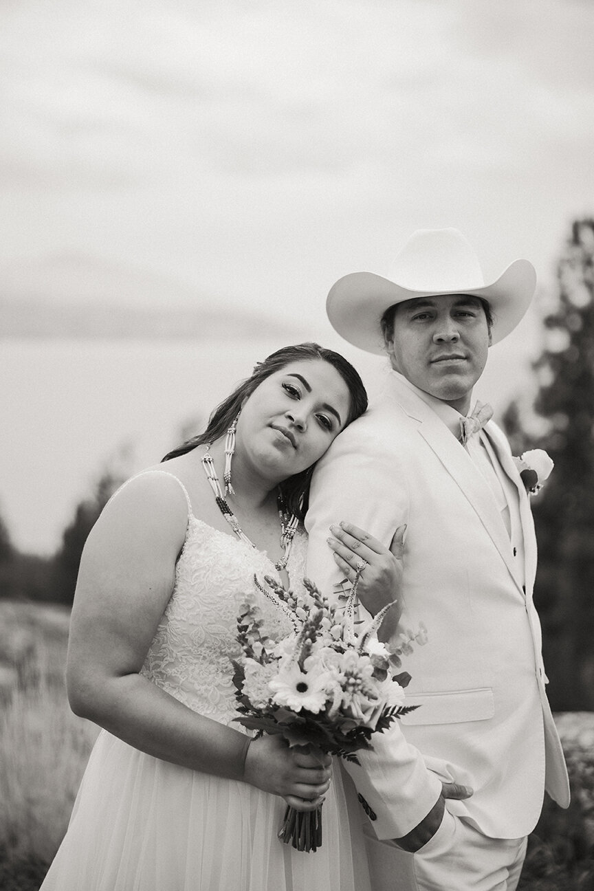 Black and white wedding portrait of a couple in a field, leaning together in a quiet moment.