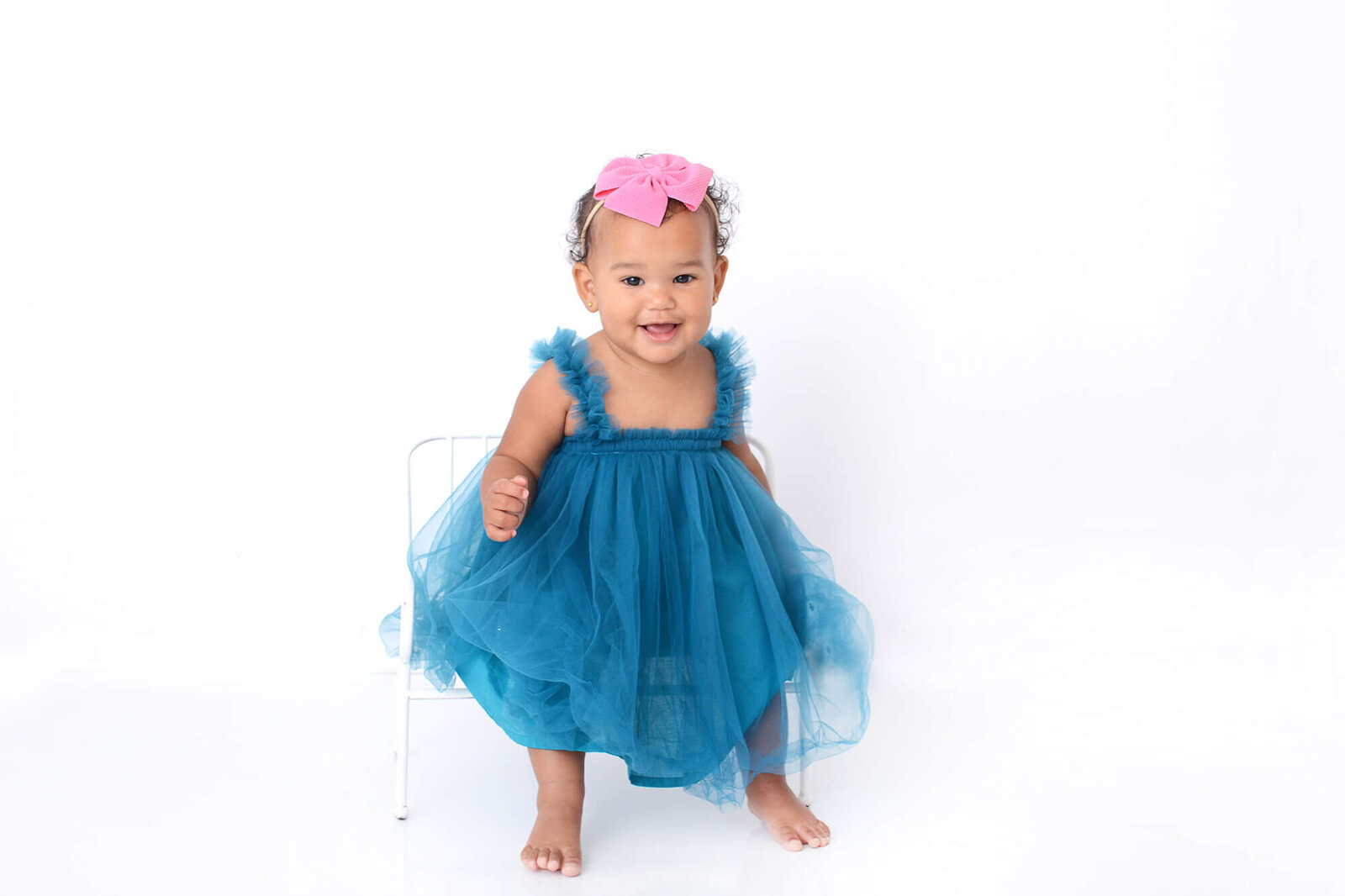 one year old girl smiles at the camera while wearing a light blue dress