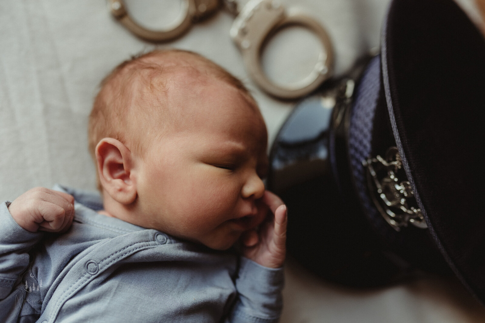 a newborn boy laying on his back, facing his fathers michigan state police hat and handcuffs