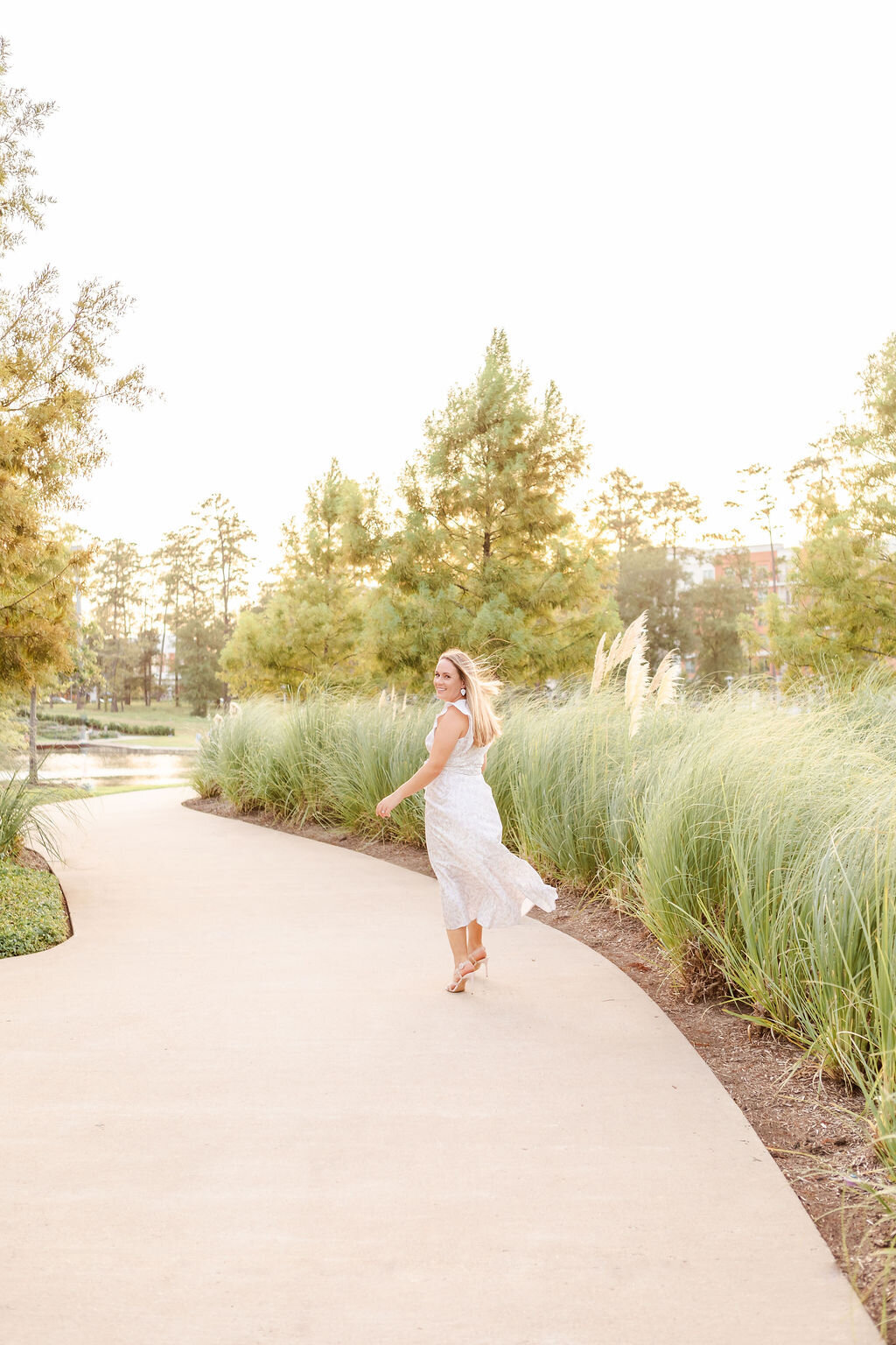 maternity session at city place in spring, tx of woman in flowy dress walking way from camera as she turns to smile back
