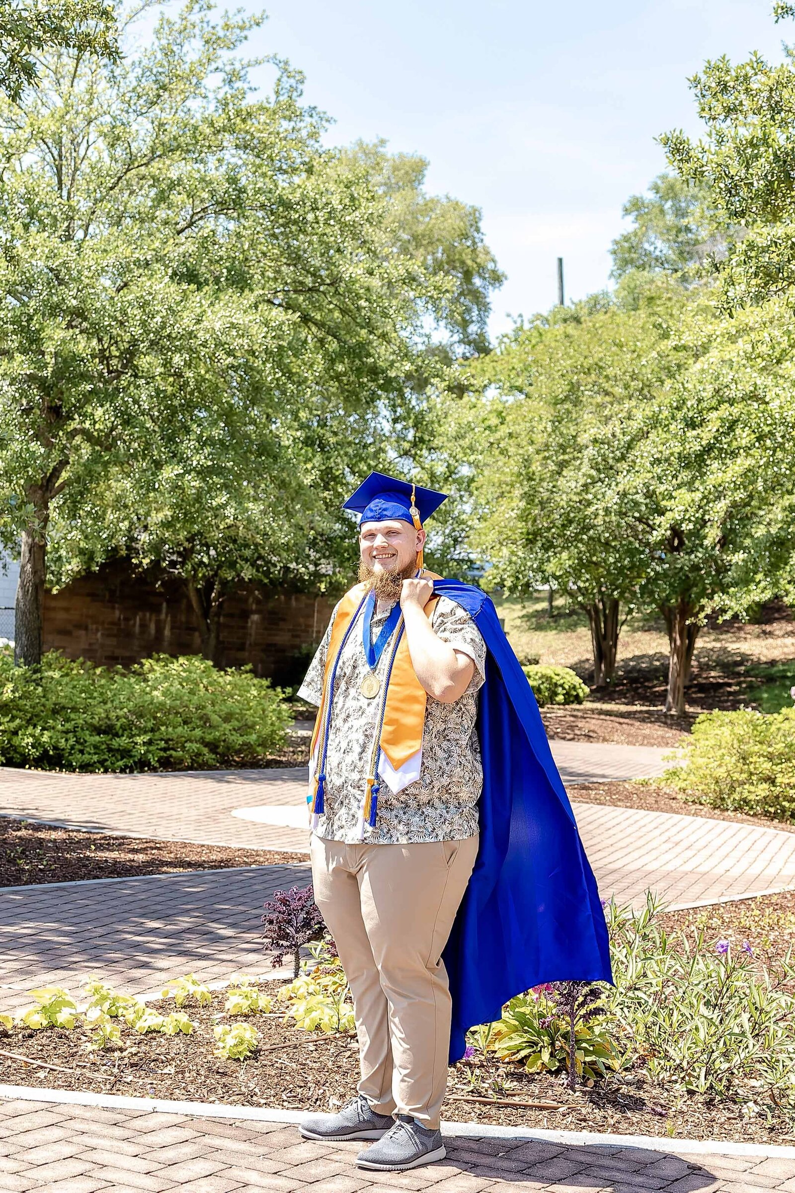 A CFCC senior in a blue cap and gown standing proudly on a campus path in Wilmington, North Carolina. This photo highlights graduation excitement and achievement, ideal for capturing vibrant senior photography in a scenic setting.