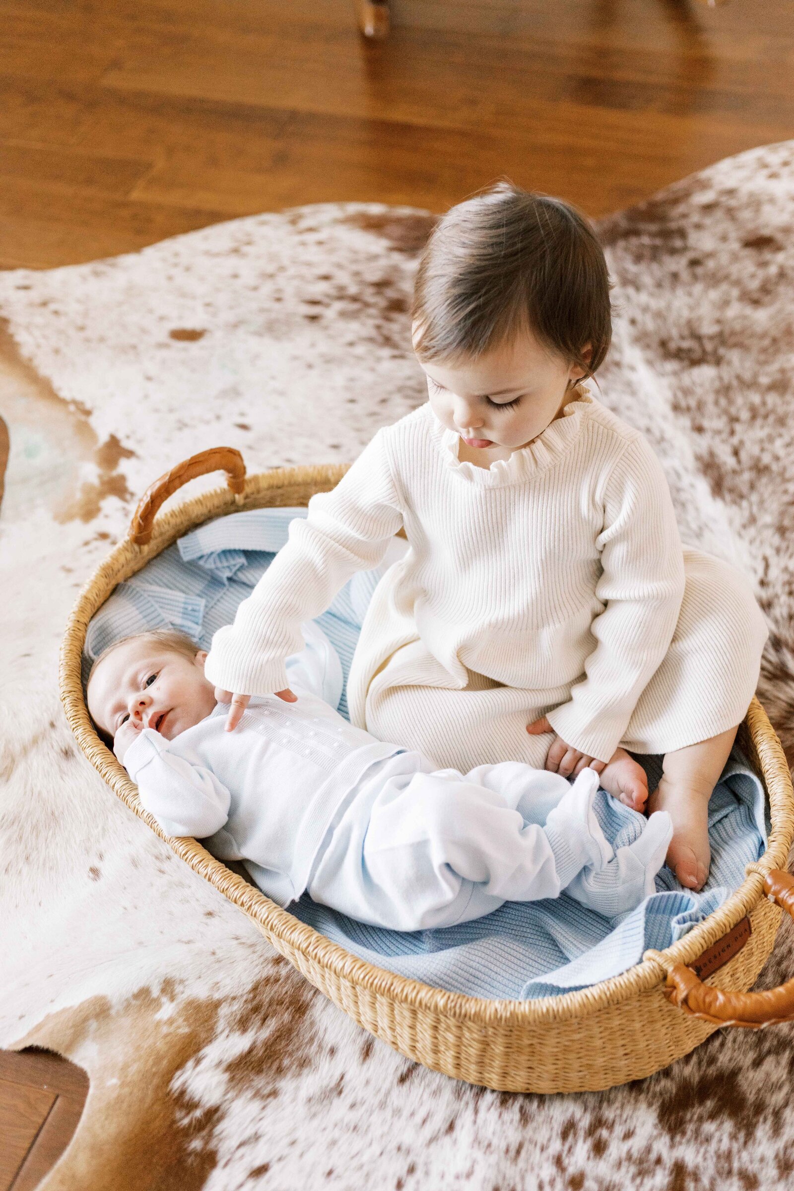sister sitting in moses basket with baby during peoria illinois newborn photos 