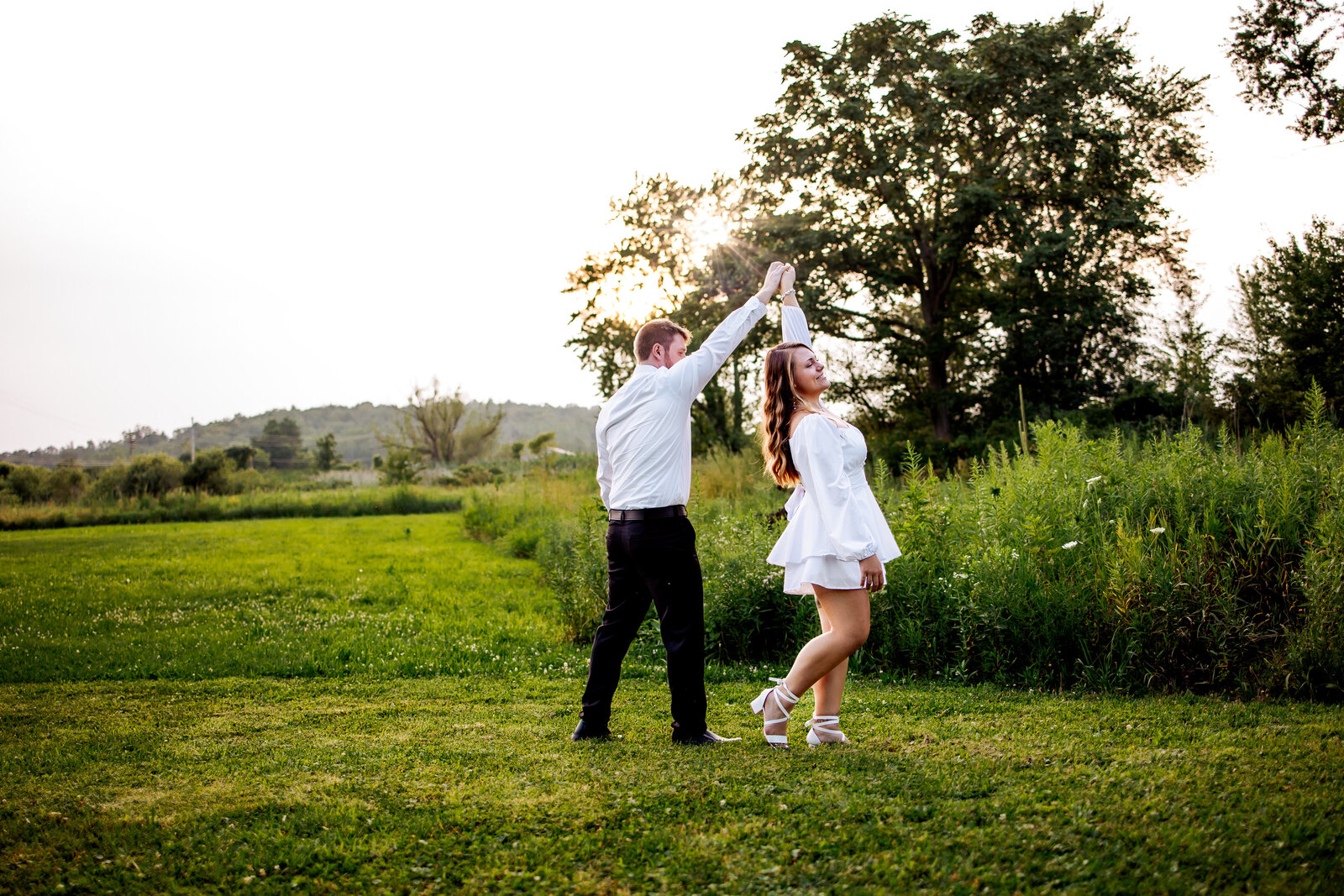 Couple shares a quick dance in a grassy field as the sun is setting