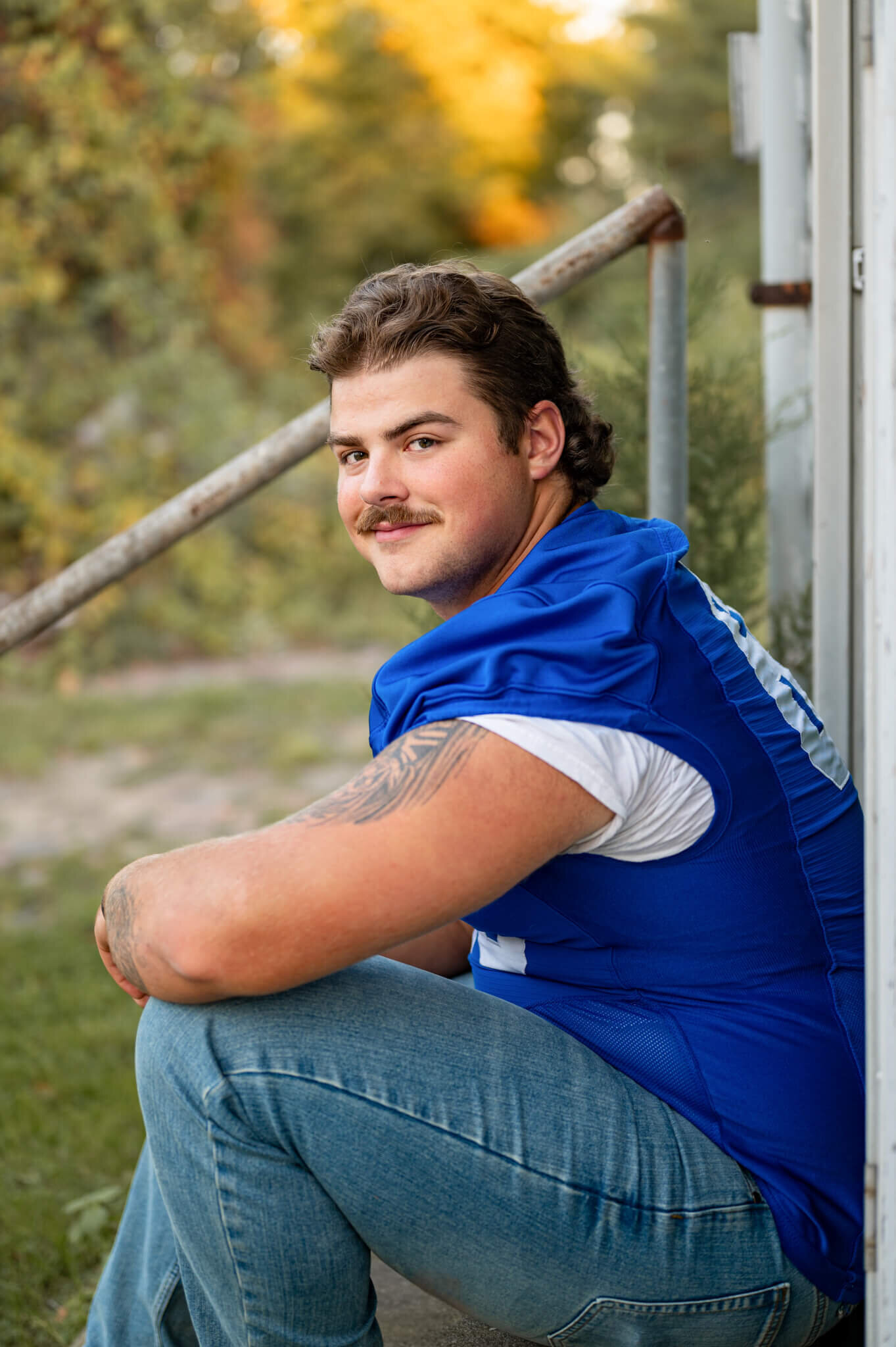 Young guy sitting on a porch smiling at the camera while wearing a blue football jersey at a park in Michigan