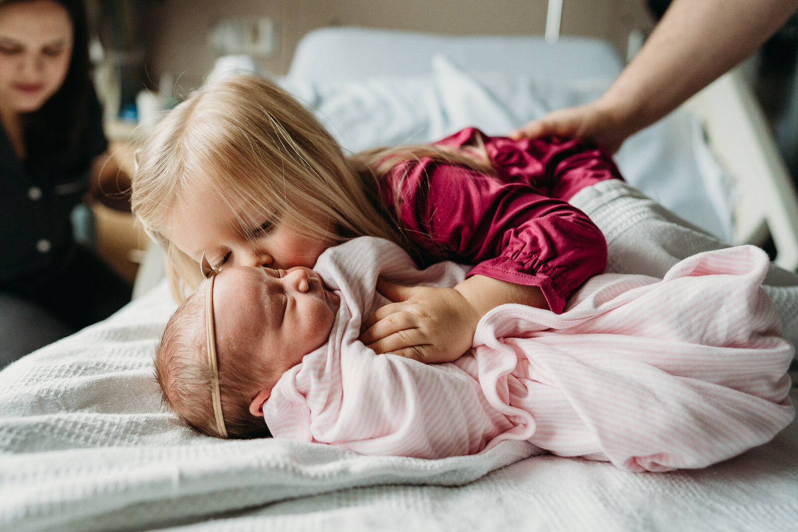 toddler girl hugs new baby sister in hospital bed