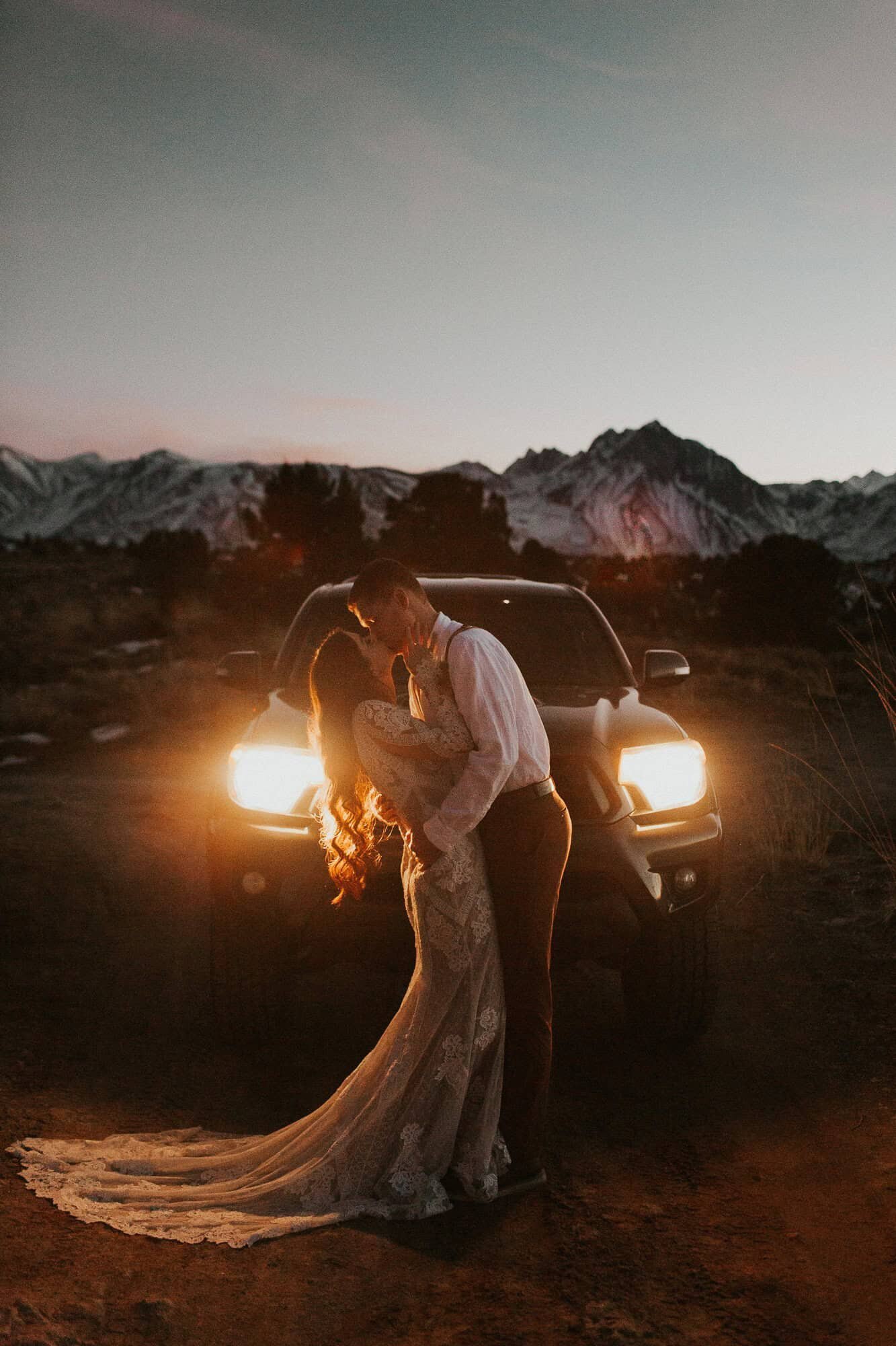A bride and groom kiss at dusk, while in the light of their Toyota truck headlights, while on their wedding day in Mammoth Lakes. 