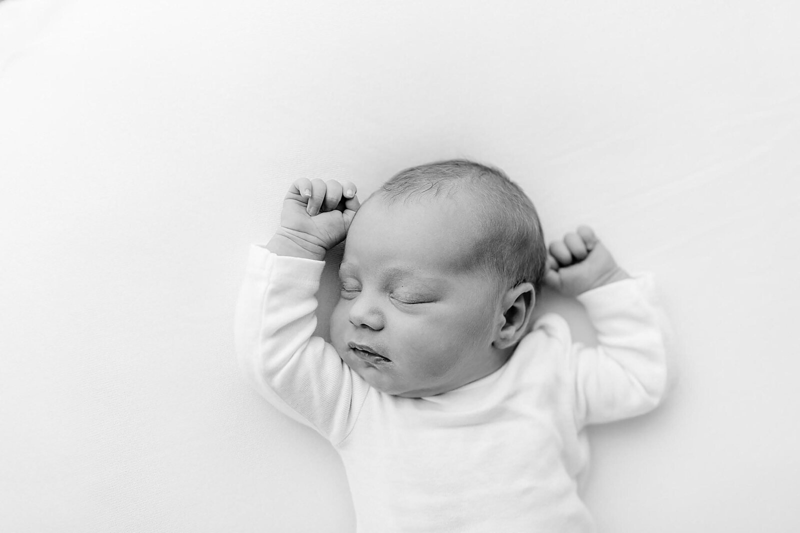 a classic black and white photo of a newborn sleeping on their back with their arms up