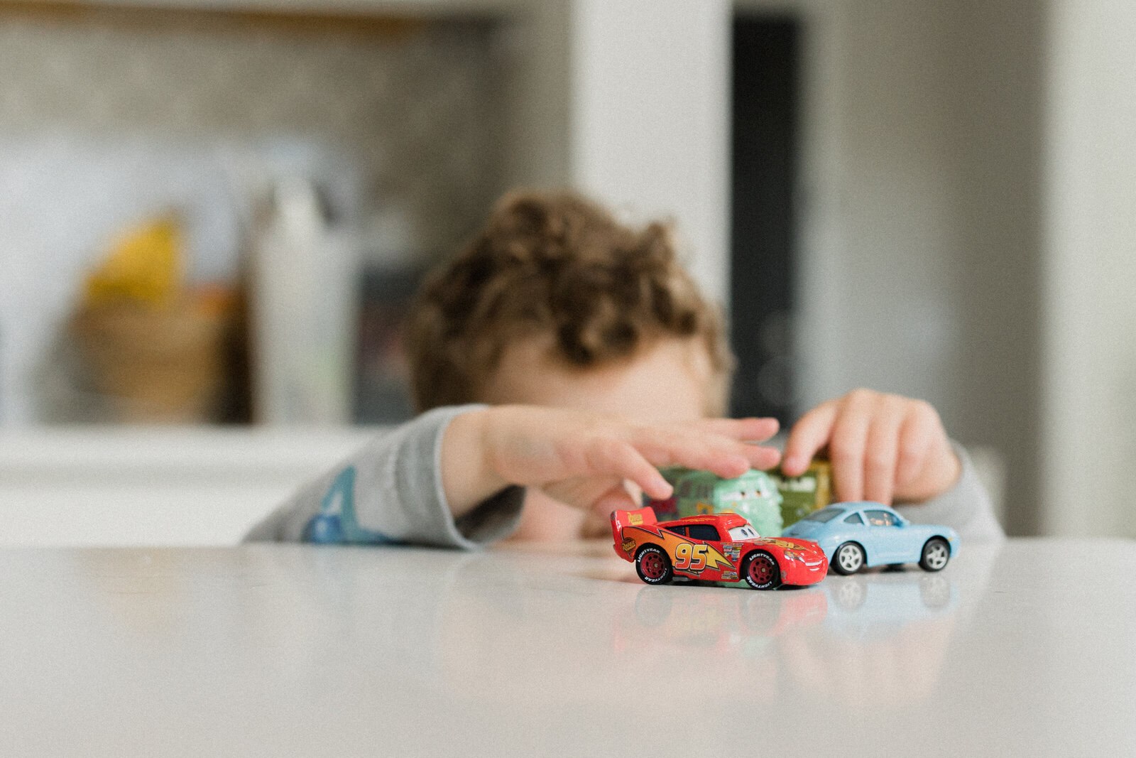 Tiny hands reach up onto the counter to grab some toy cars