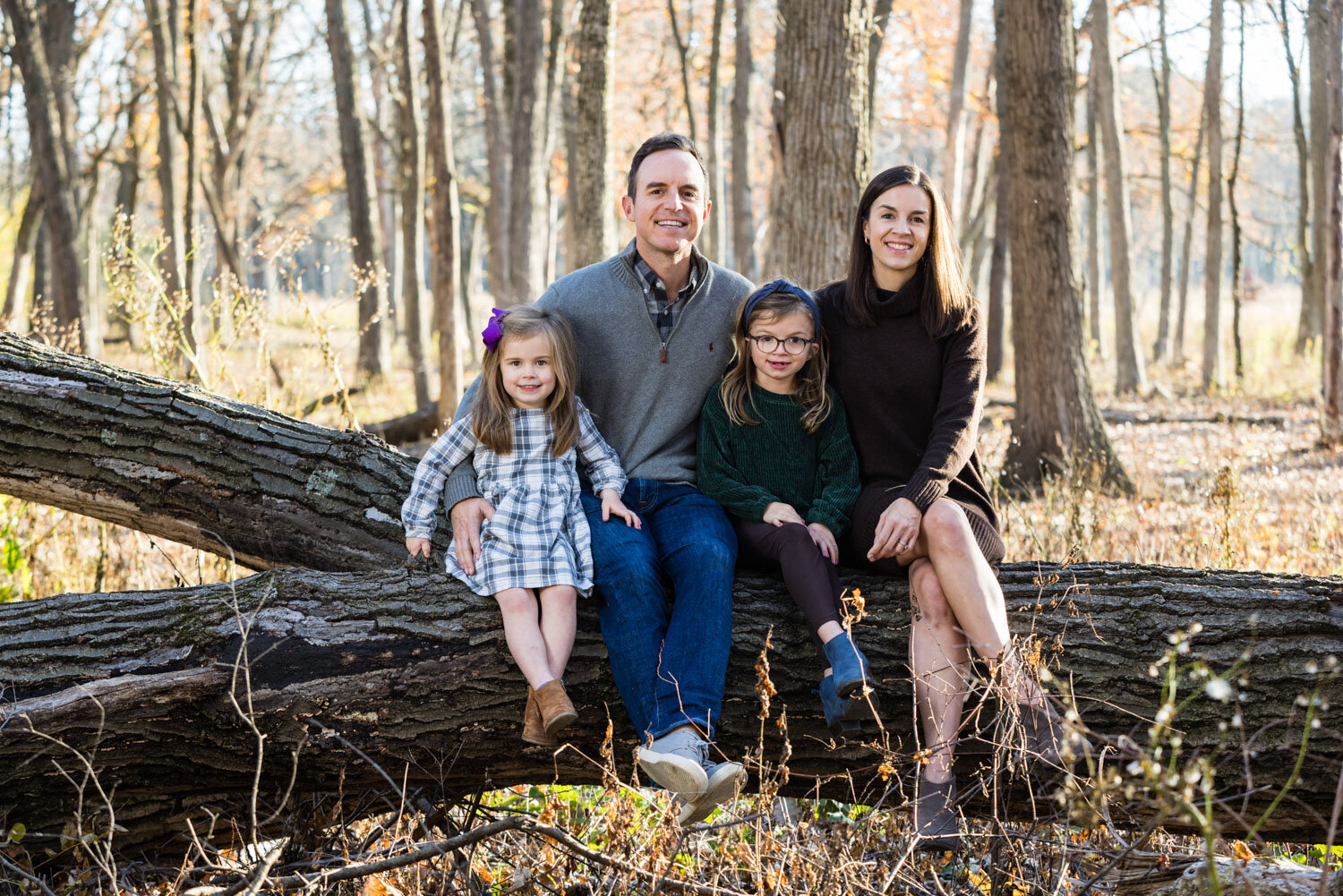 A family is sitting on a log in the woods.