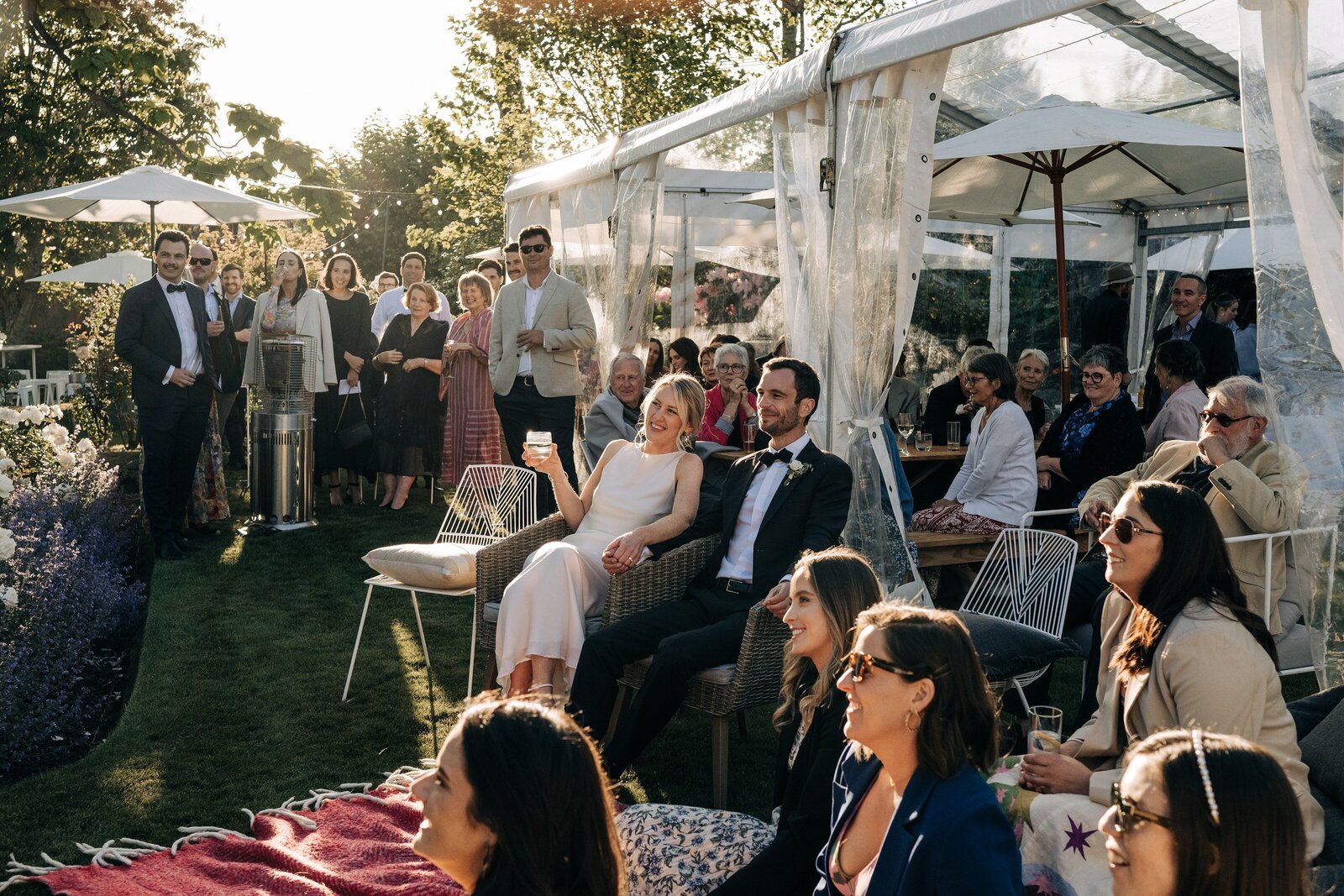 a bride and groom sitting on the lawn in front of a clear marquee in their backyard wedding in merivale christchurch