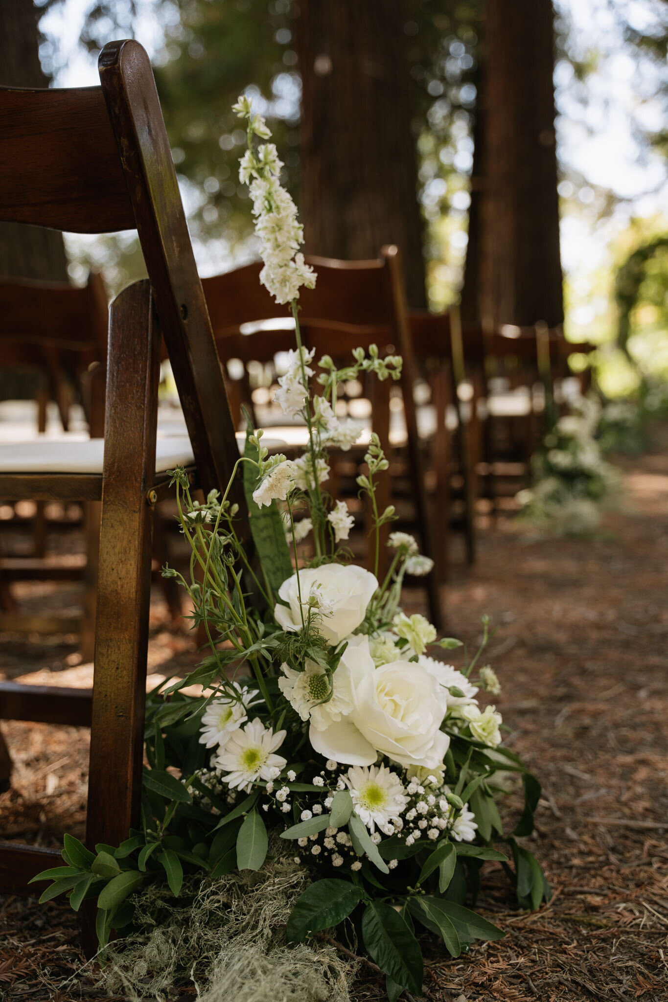 White florals and wooden chairs under towering redwoods for outdoor wedding ceremony in Northern California