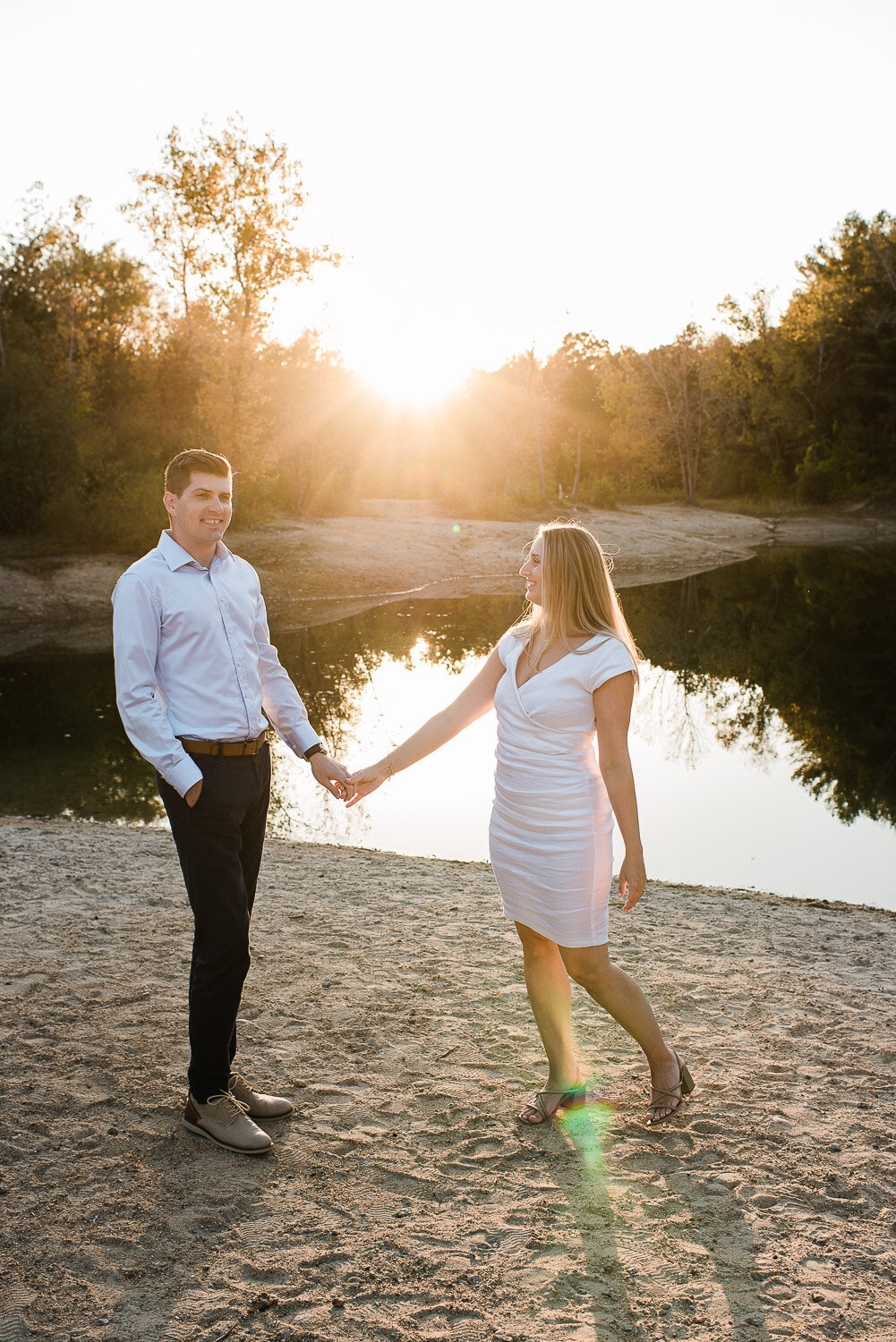 couple hold hands standing by water in sunset