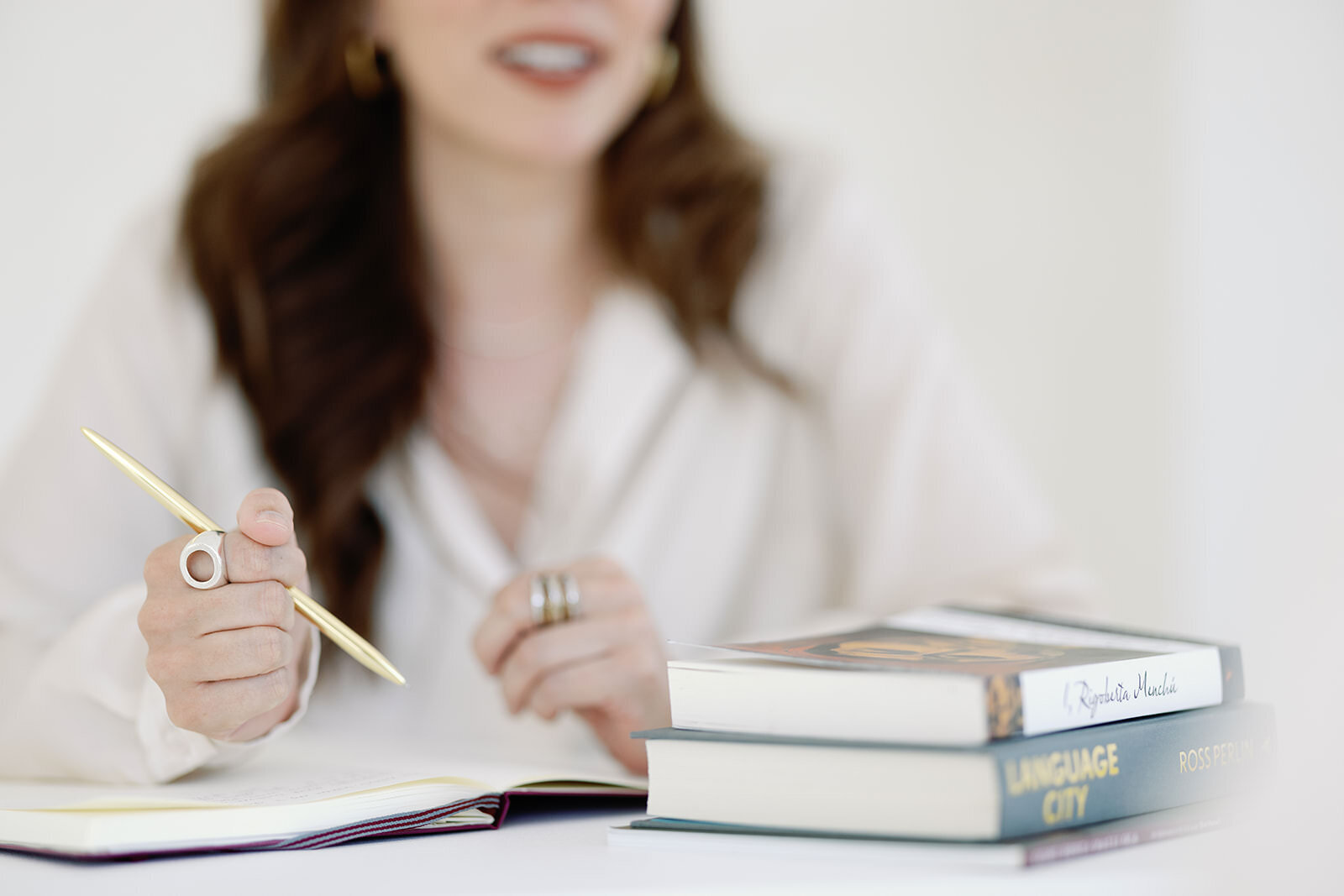 Lifestyle headshot featuring a woman holding a pen with books in the background, conveying thoughtfulness and expertise.