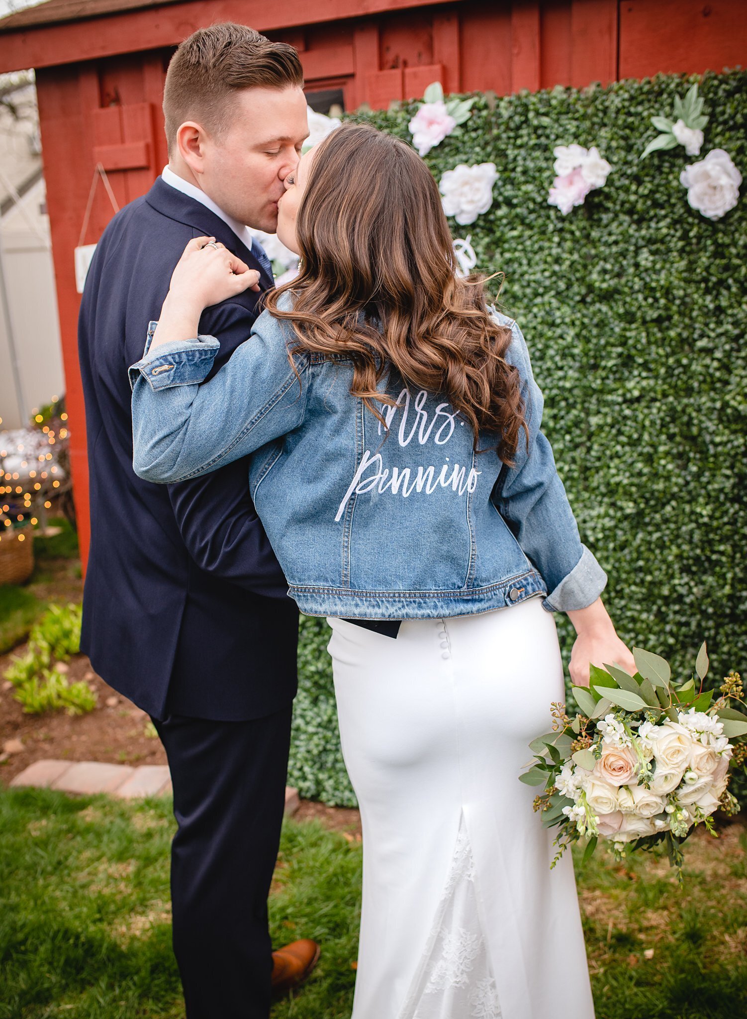 bride in jean jacket kissing groom at intimate wedding