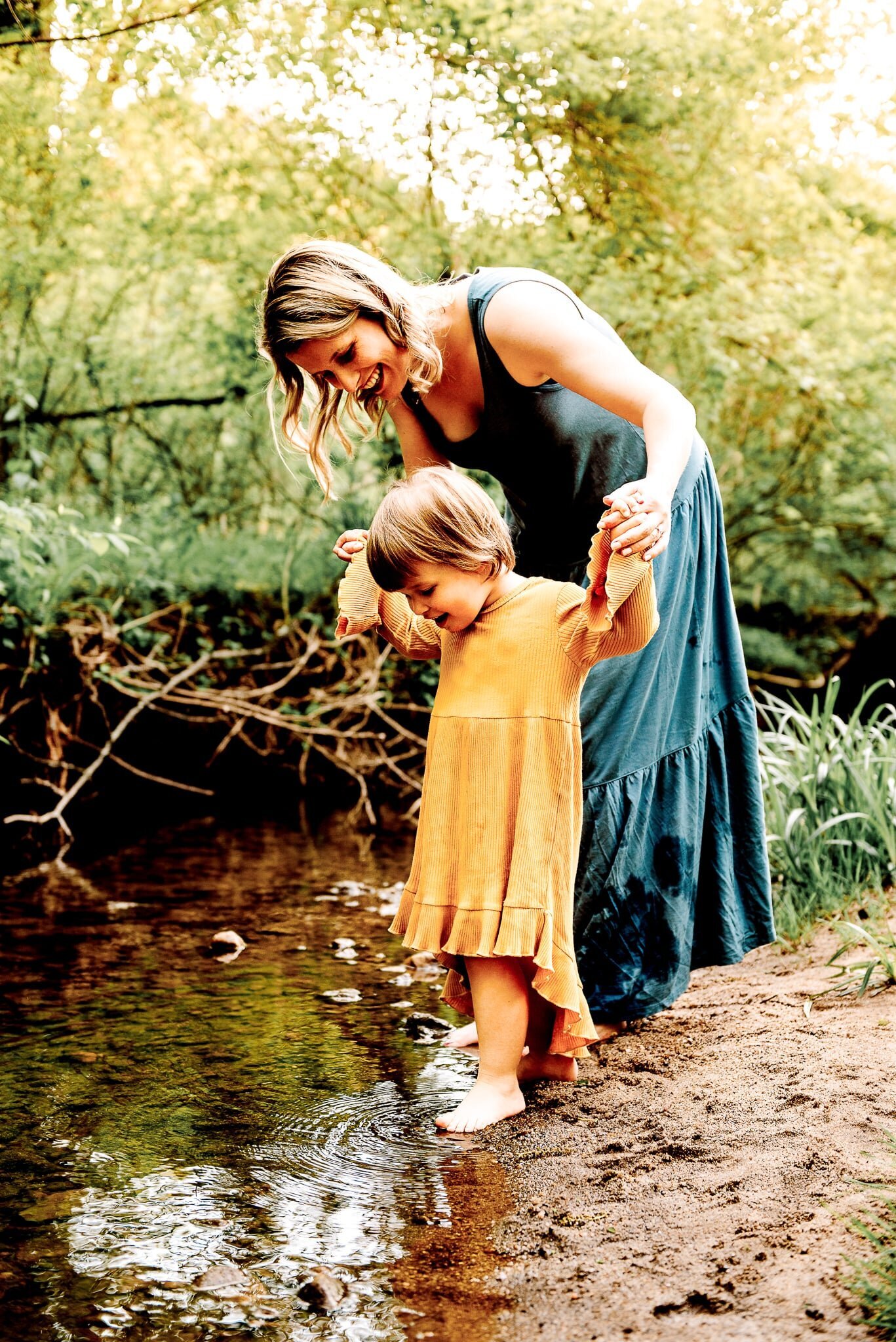 mom holding daughters hand while playing in creek