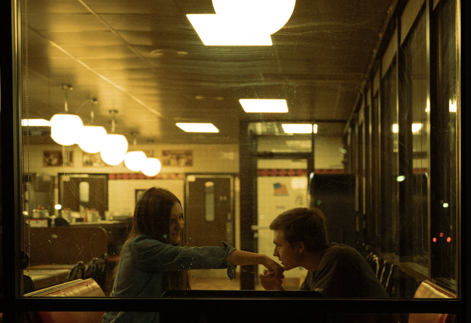 A couple on a date at their favorite restaurant. They're sitting in a booth and he is kissing her hand from across the table.
