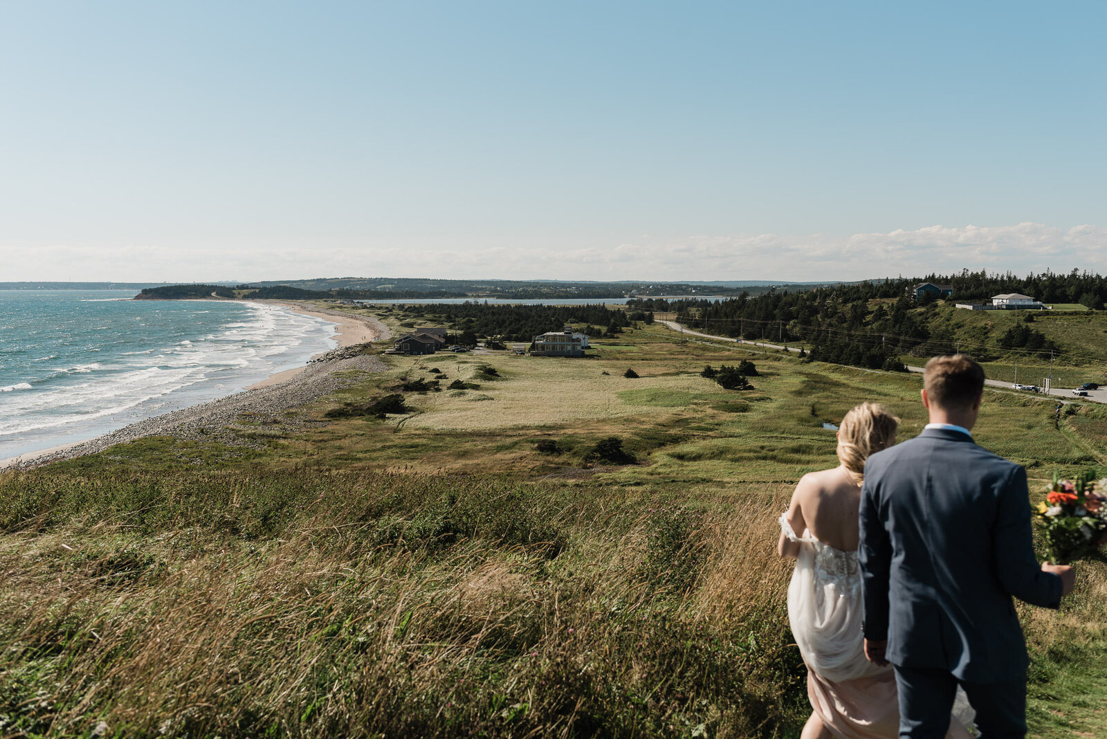 Wedding couple standing in beautiful Nova Scotia landscape with Atlantic Ocean backdrop.