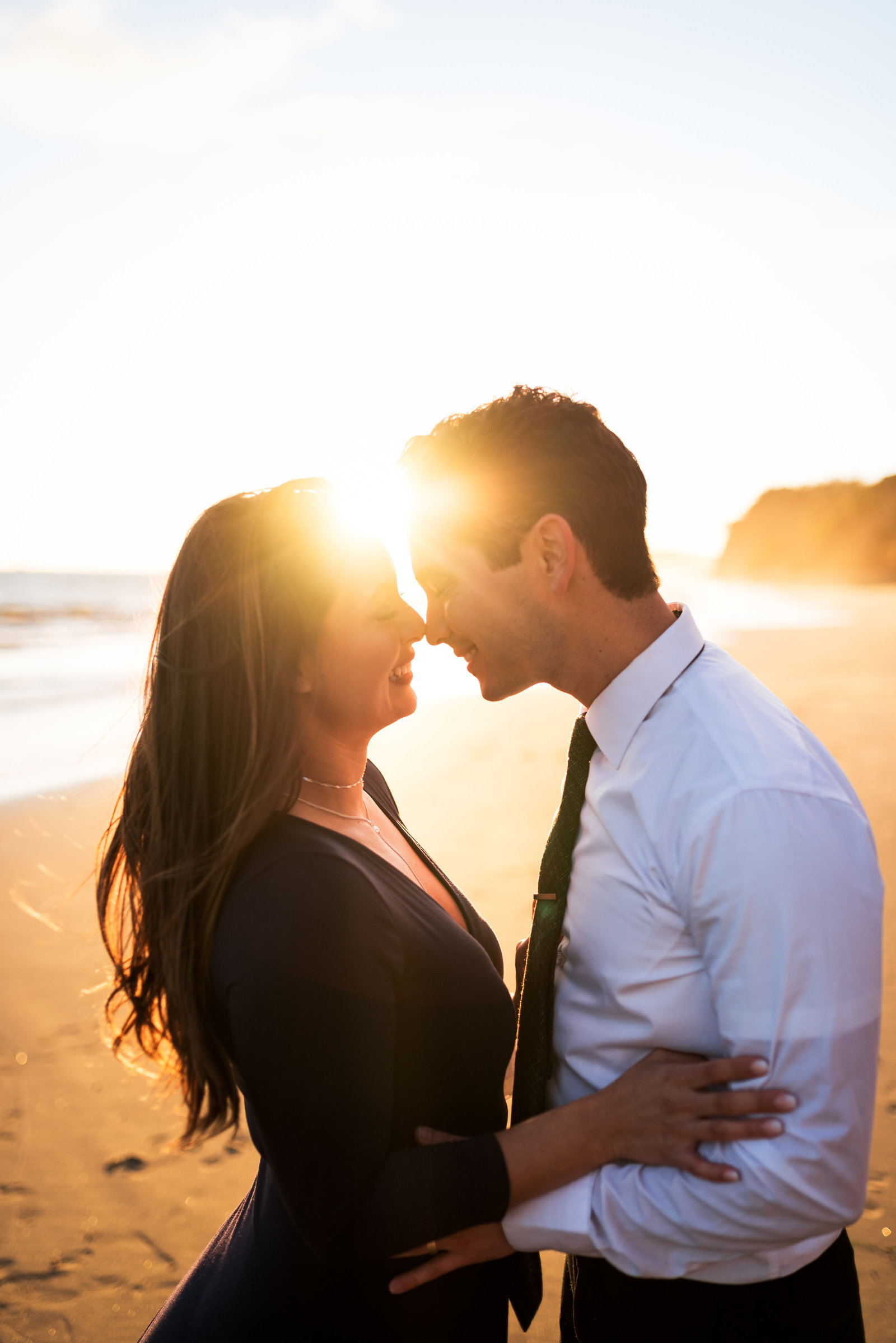 Couple in nice attire touching noses and smiling with eyes closed.