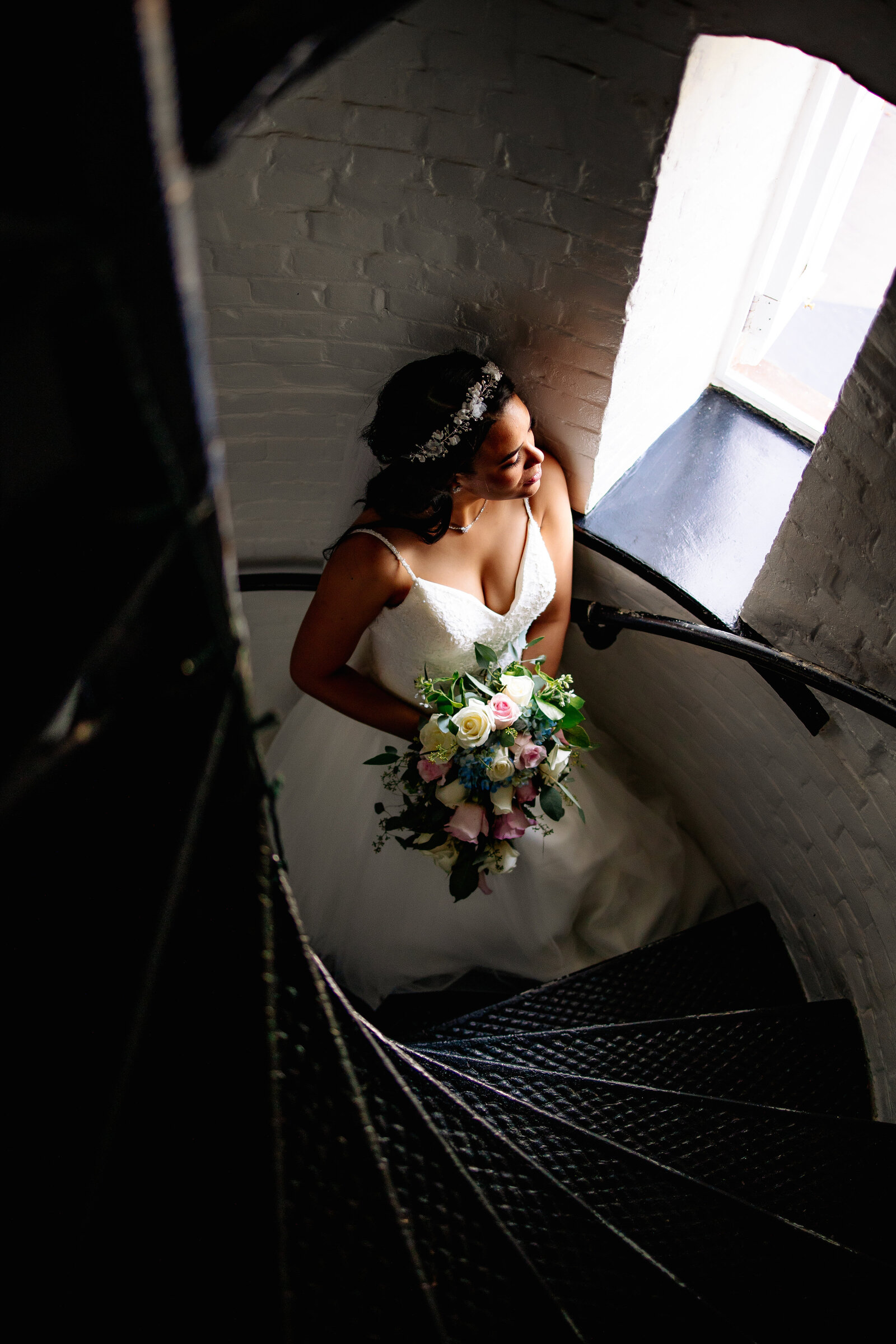 While walking up the stairs, bride stops to gaze of the window  of the lighthouse