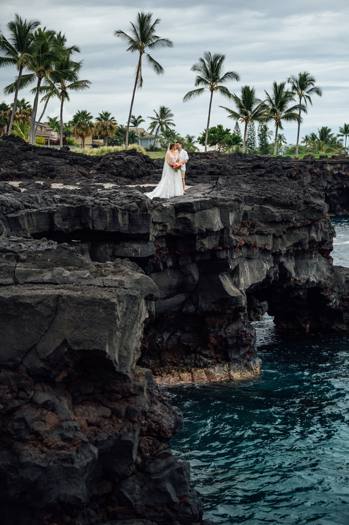 couple on a cliff of black rocks during their big island wedding