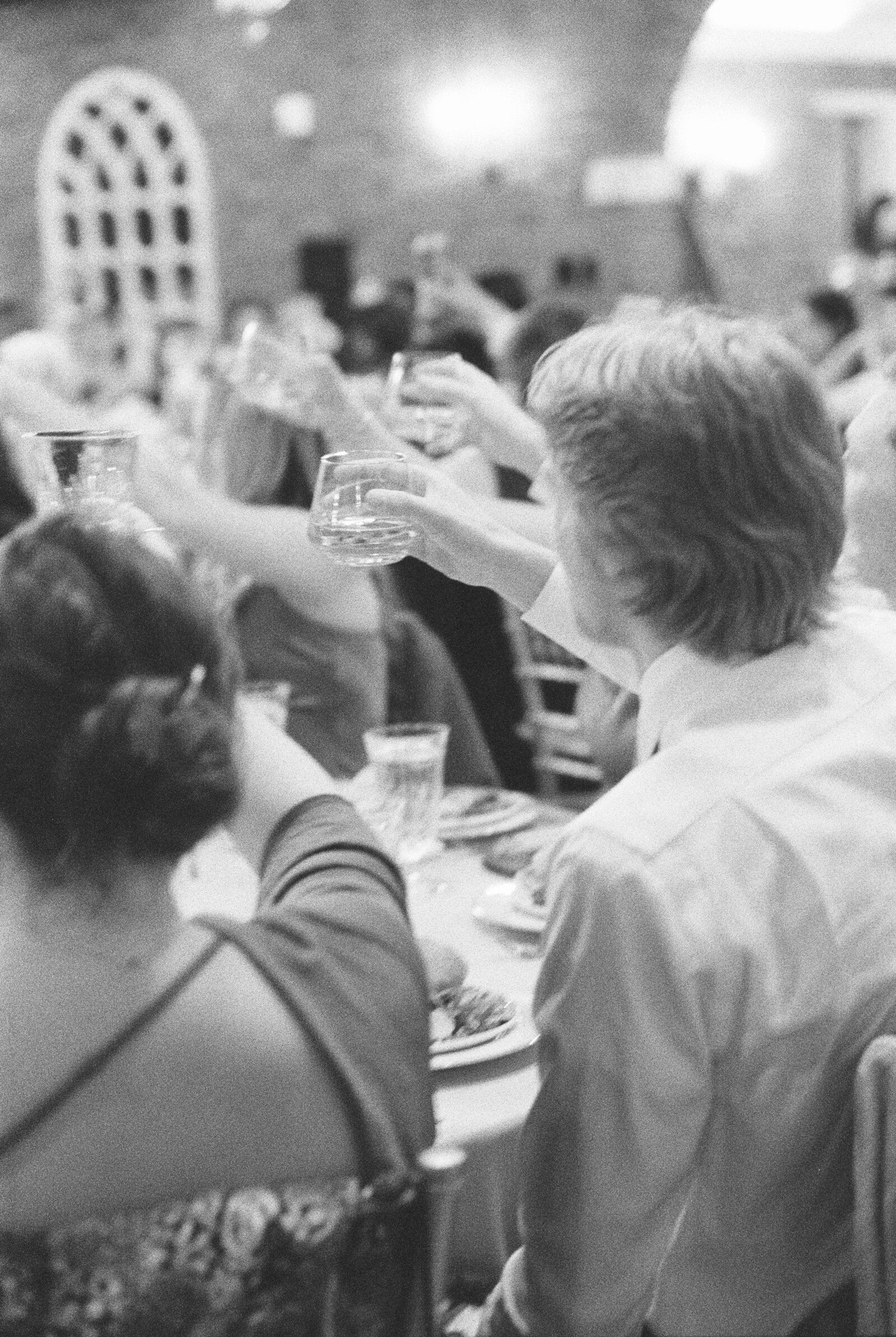 Black and white film photograph of guests raising their glasses during toasts.