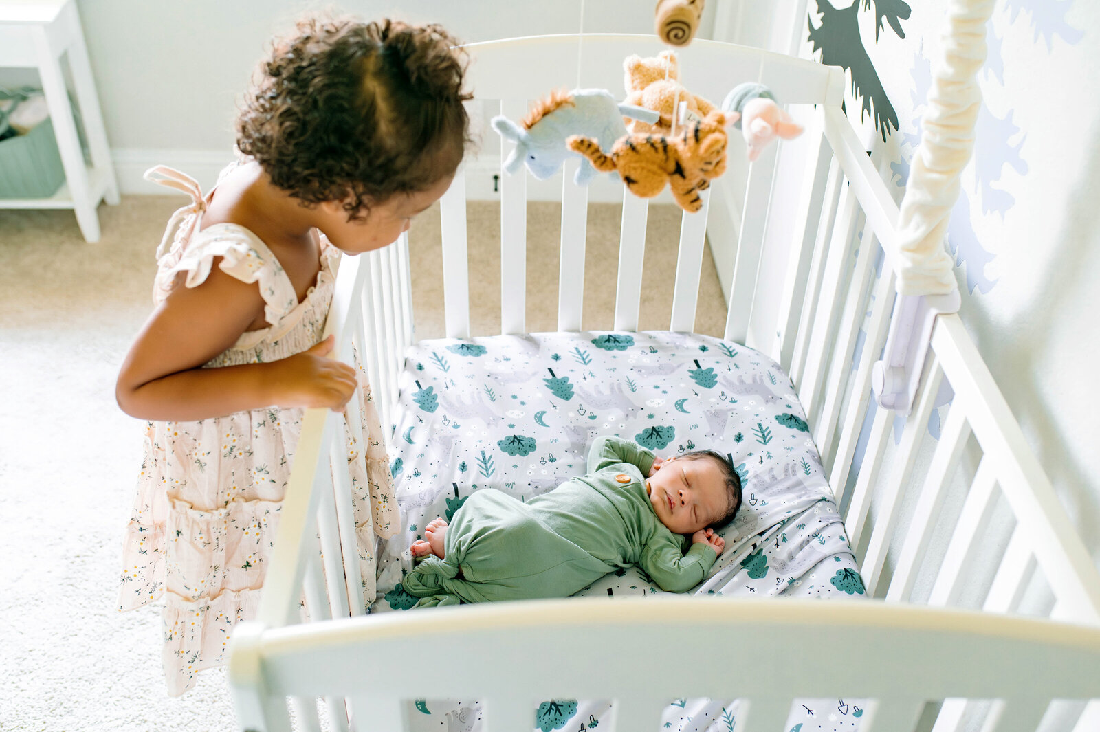 Mother leaning over crib admiring her baby during a bright, lifestyle newborn photography session in Plano, Texas, photographed by Jennifer L. Kirk Photography.