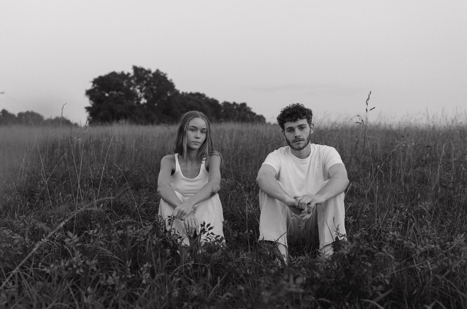 A couple posing together during a romantic photography session in a scenic field, with soft natural lighting.