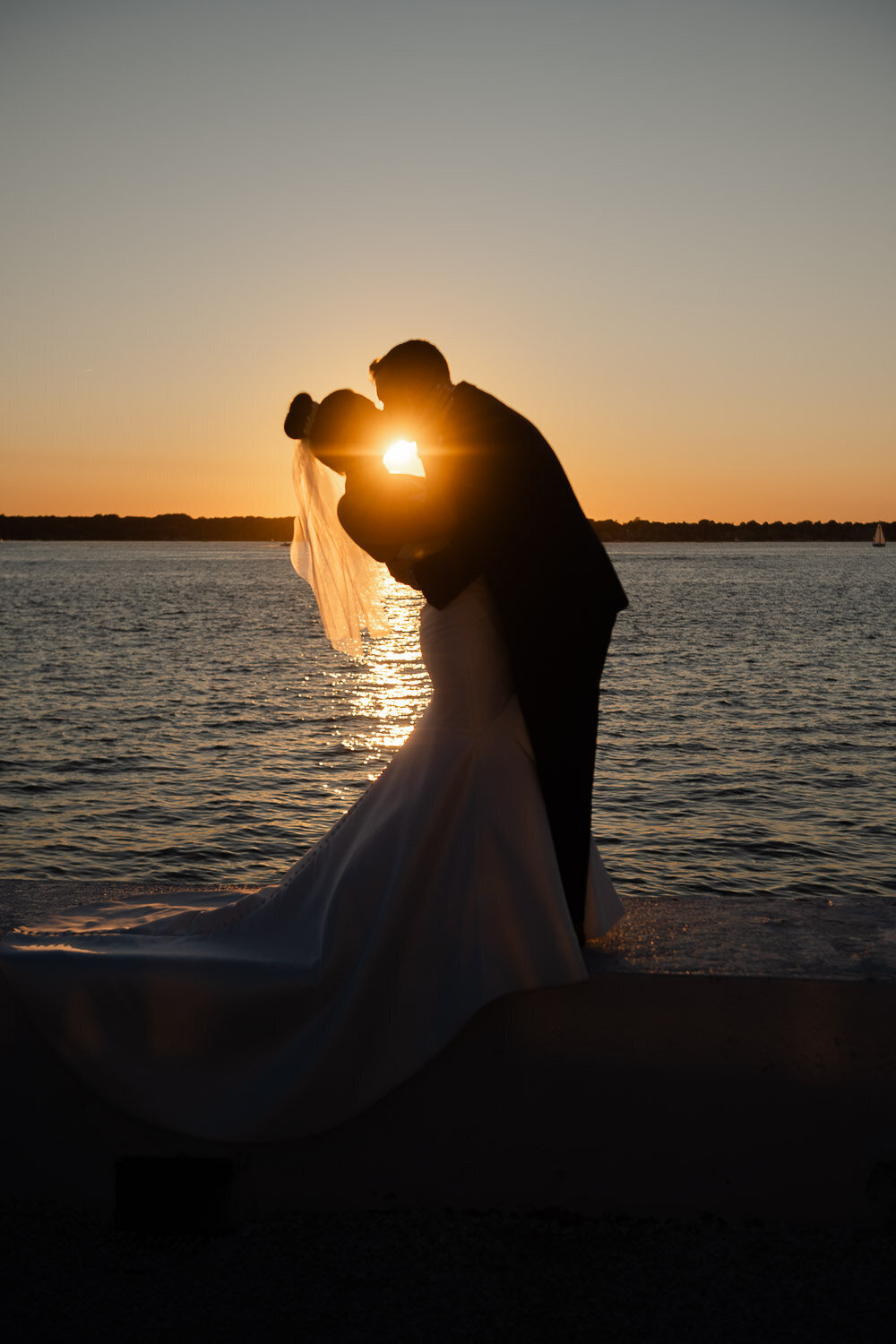 bride and groom kiss at sunset by water