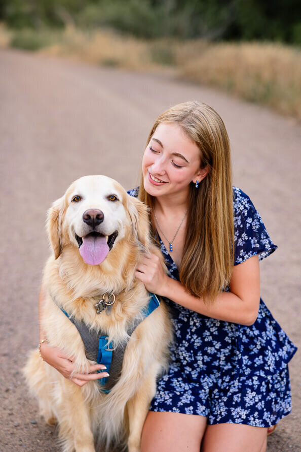 Girl in blue dress looks at her dog.