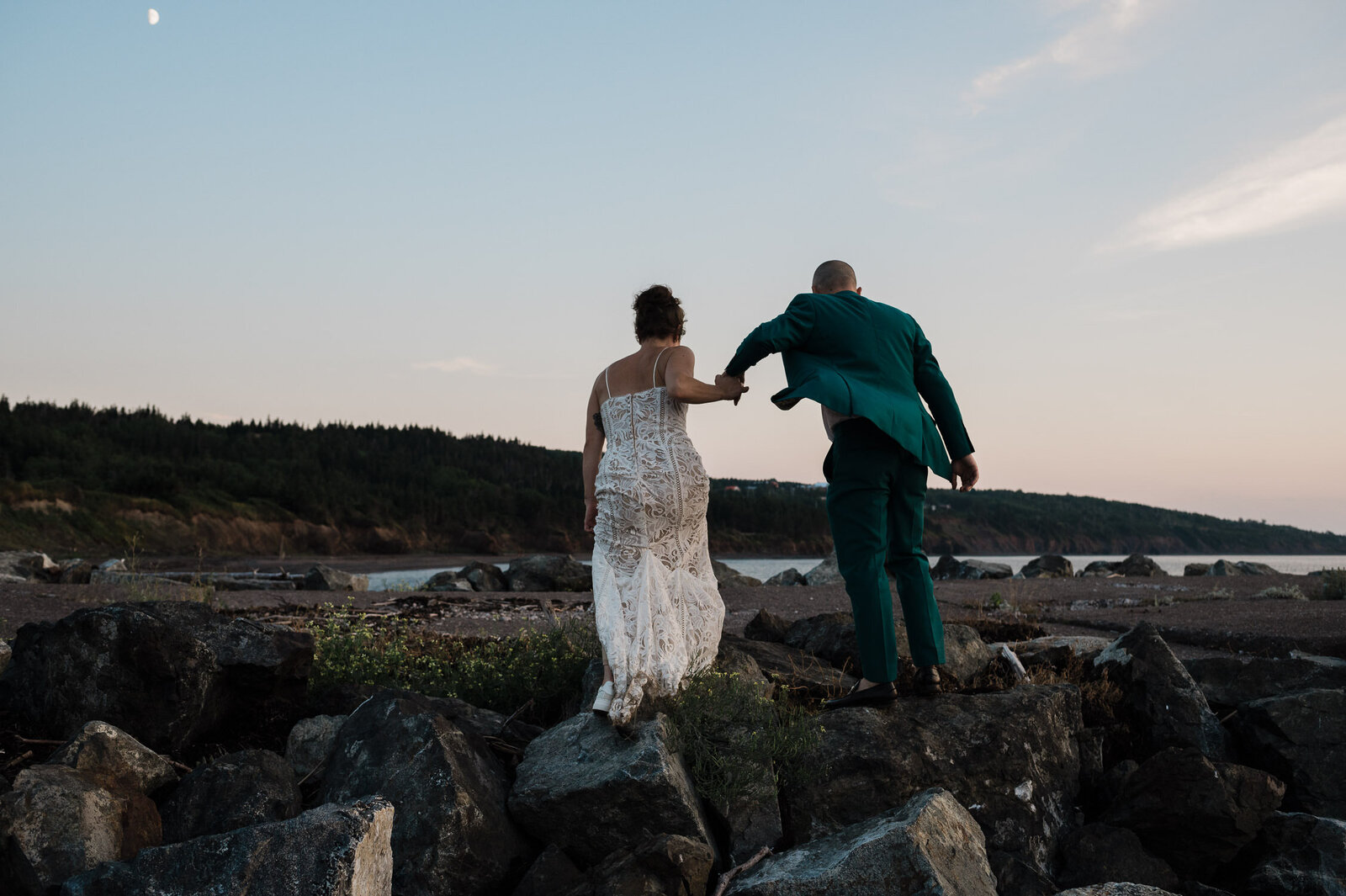 Wedding couple climbing over rocks in Lunenburg, Nova Scotia.