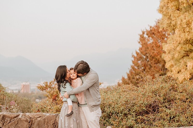 Mom and dad giving daughter cheek kisses in Queen Elizabeth Park Vancouver Family Photographer